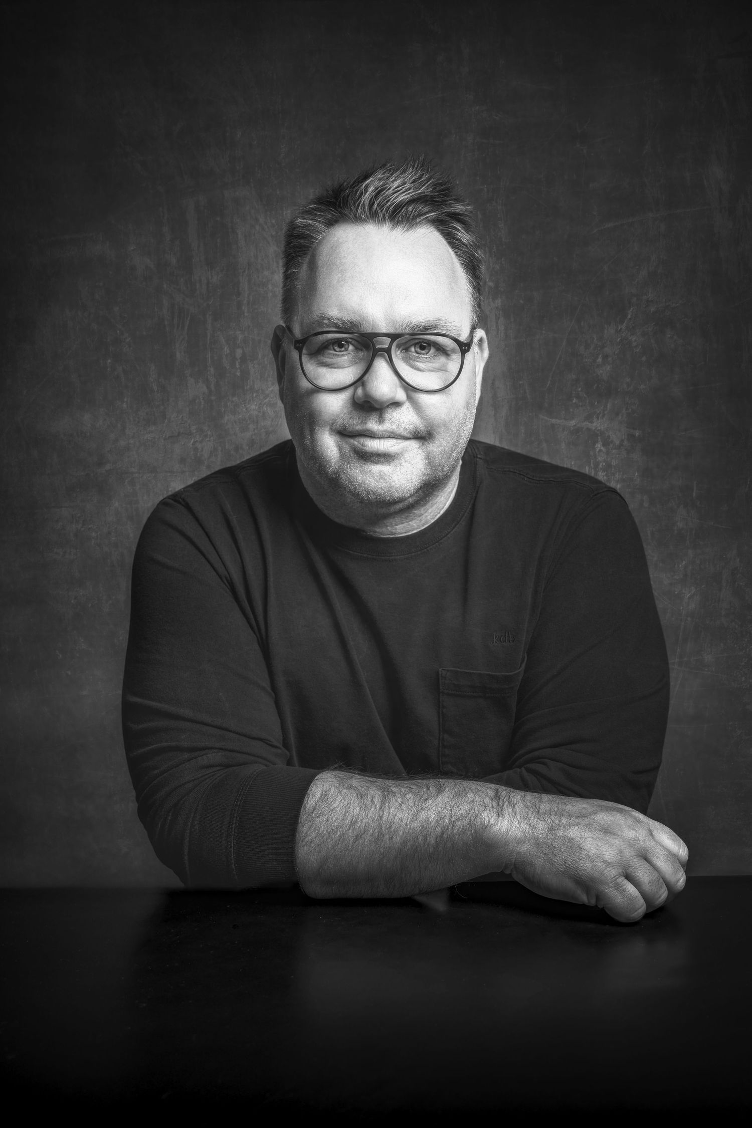 Black and white studio portrait of person in glasses and dark sweater.