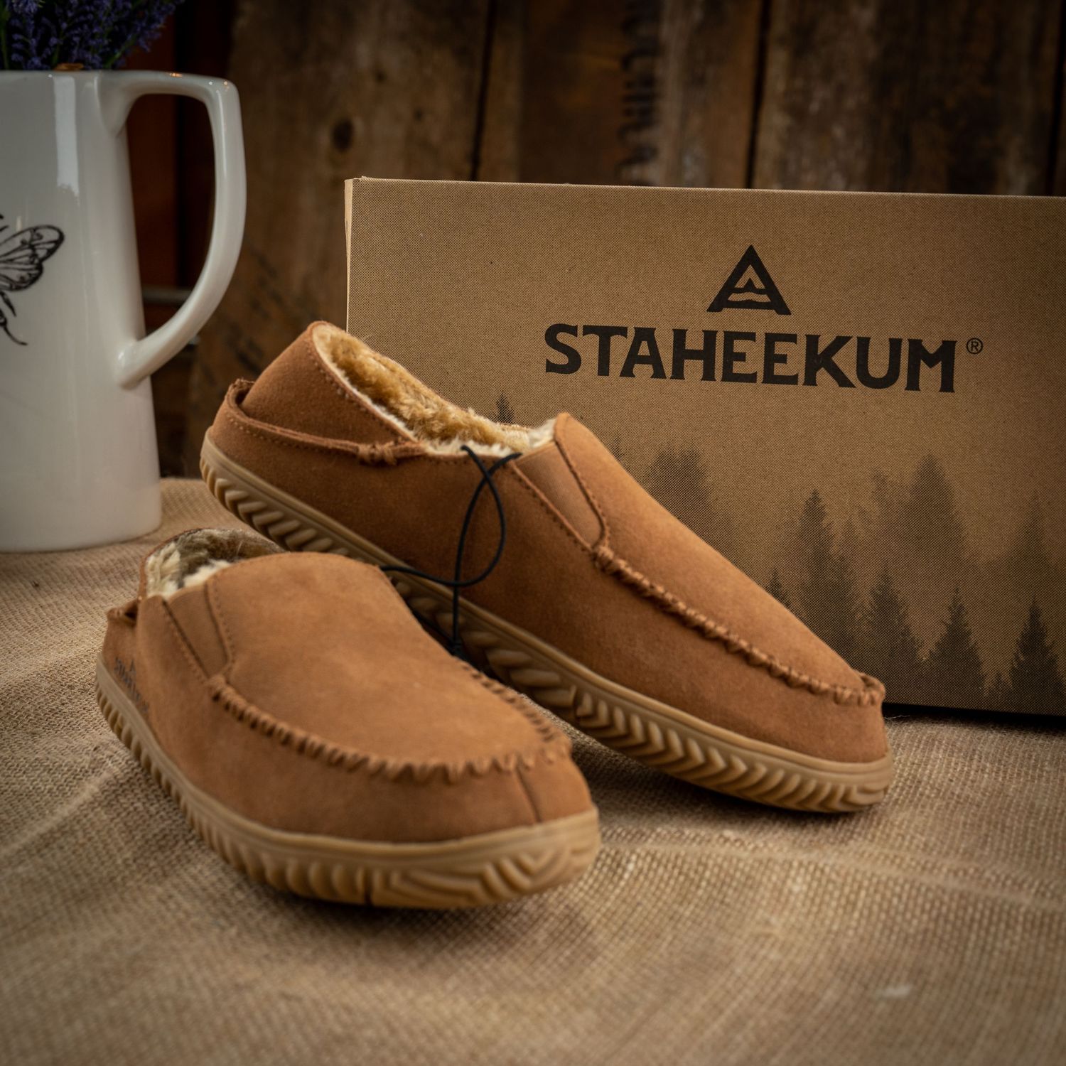 Tan suede moccasin slippers next to Staheekum branded box and decorative mug.