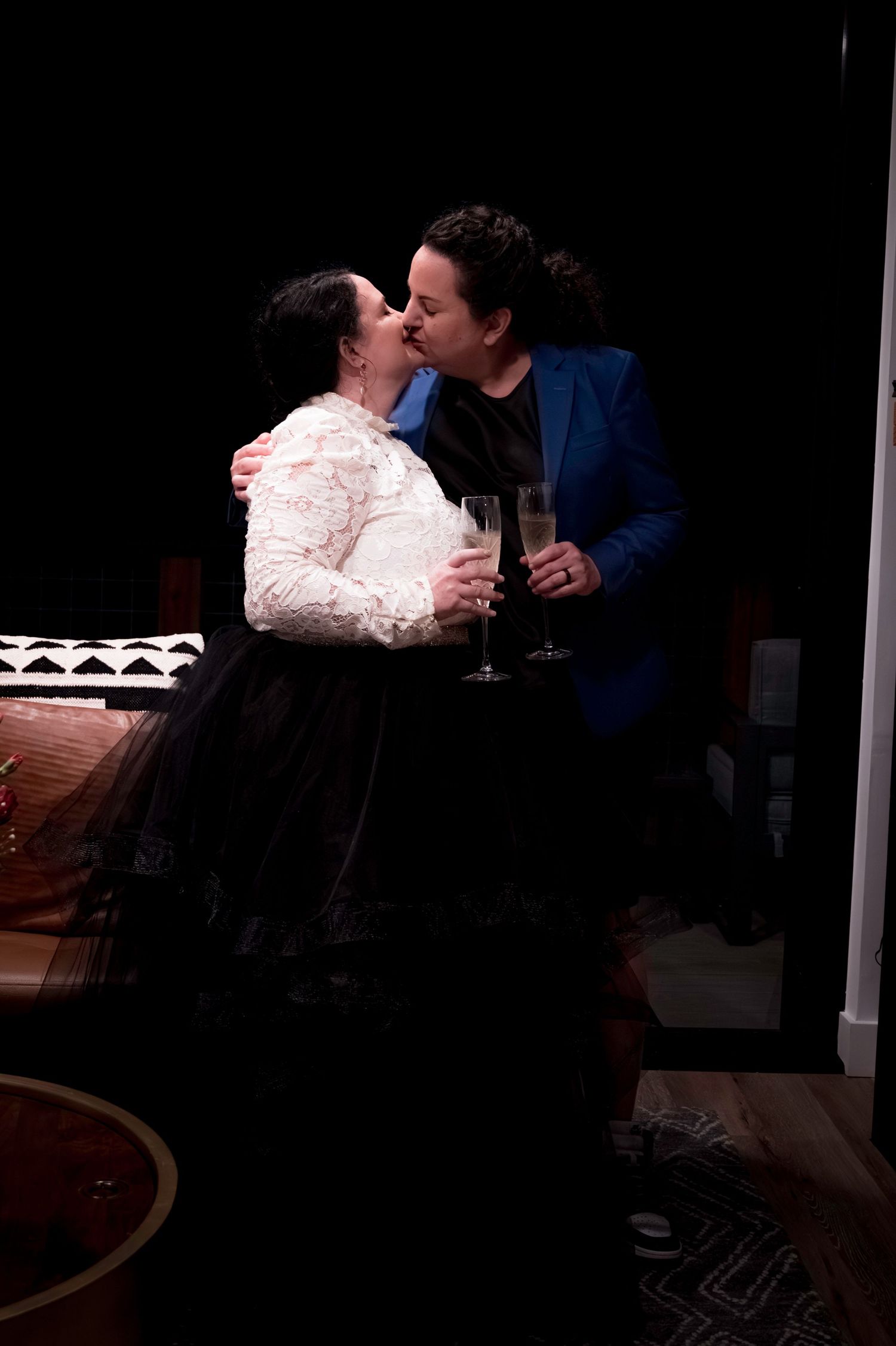 A couple sharing a celebratory toast and kiss in formal attire against dark background.