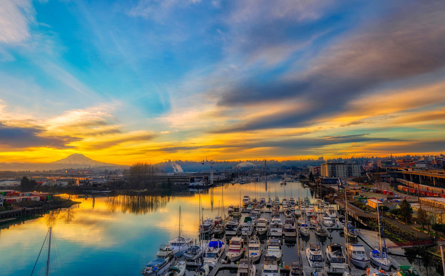 Vibrant sunset over marina filled with boats and yachts under colorful cloudy sky.