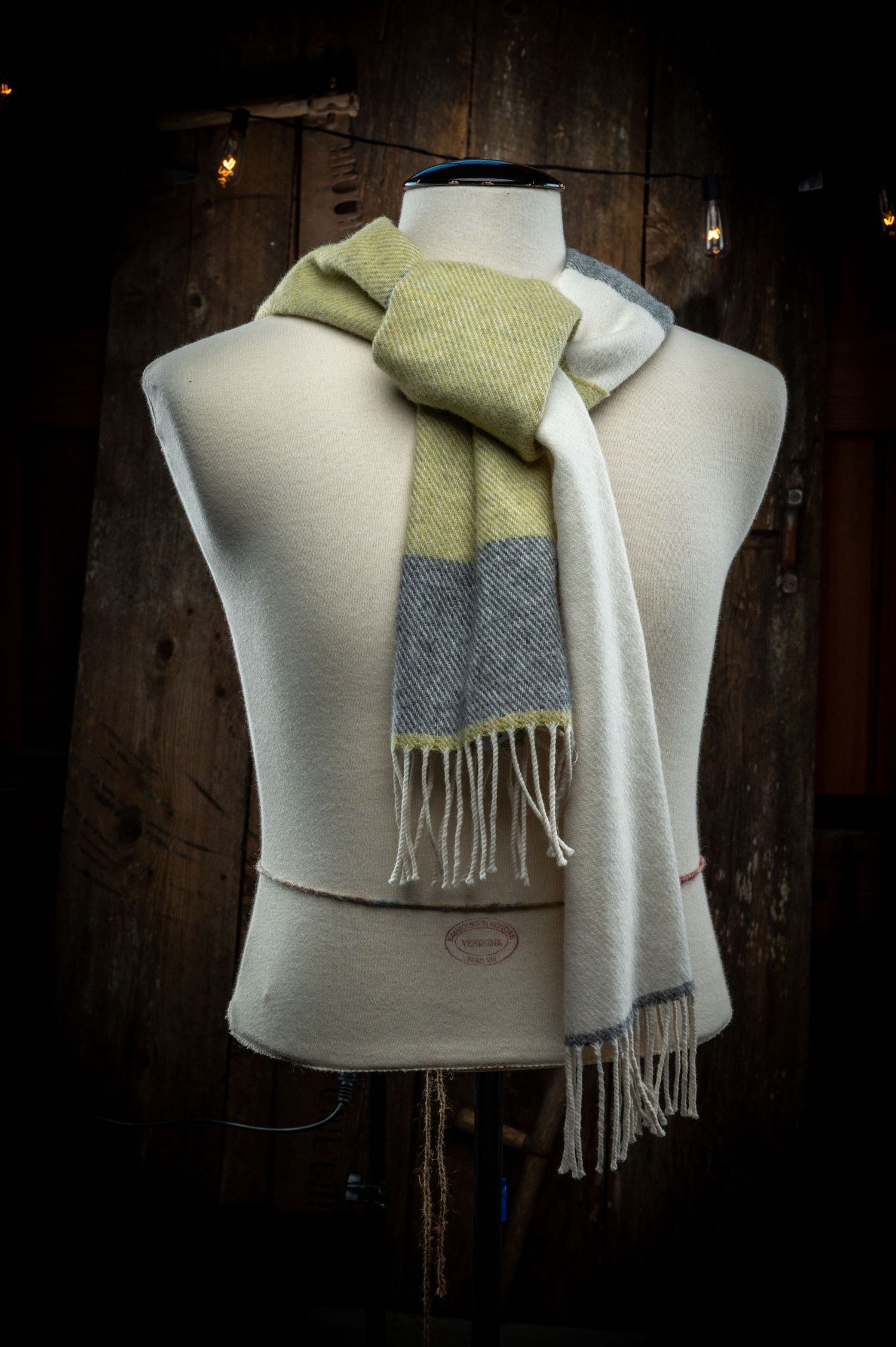 Mannequin torso displaying a striped green and grey wool scarf against dark wood background.