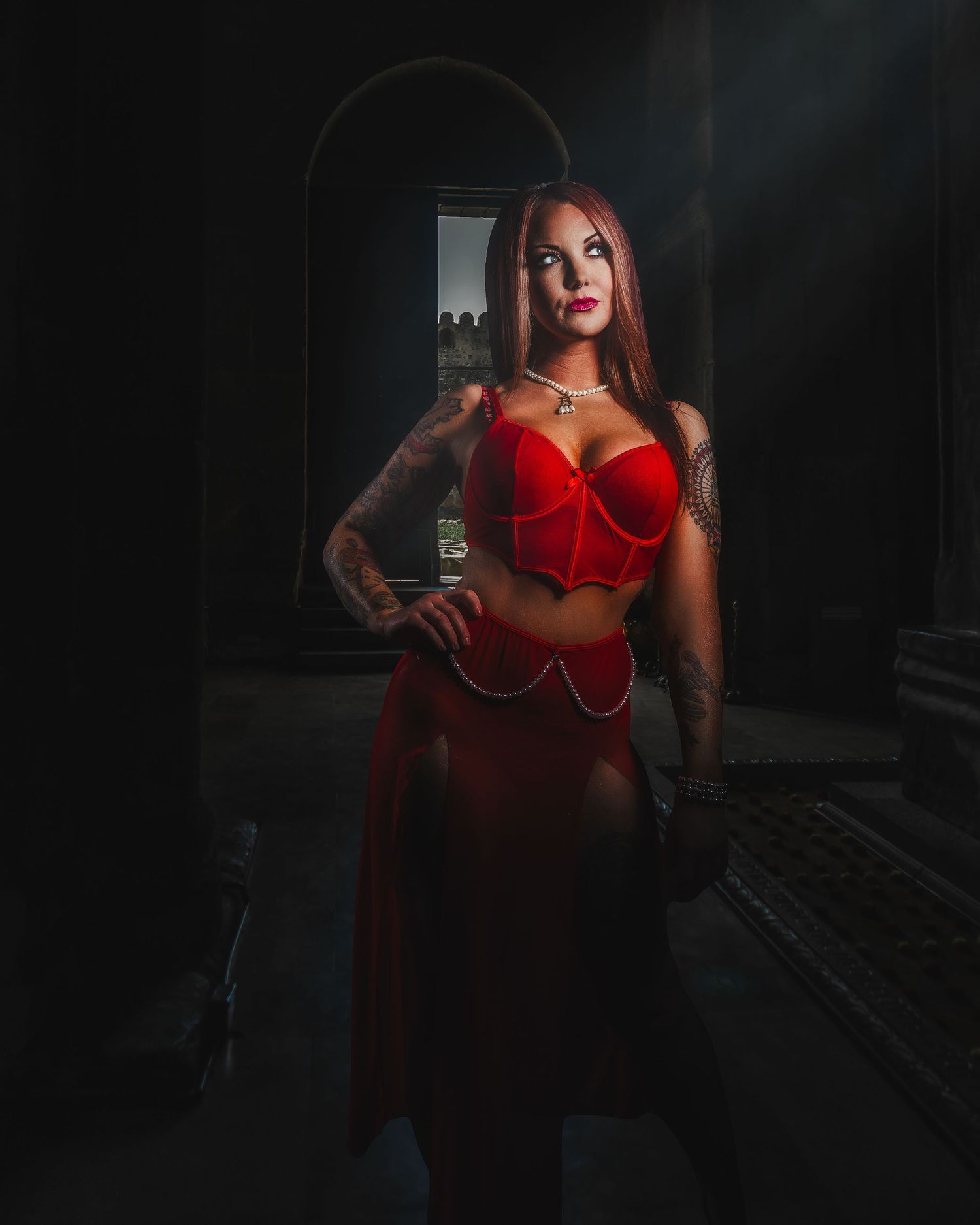 Moody portrait in red outfit against dark archway background.