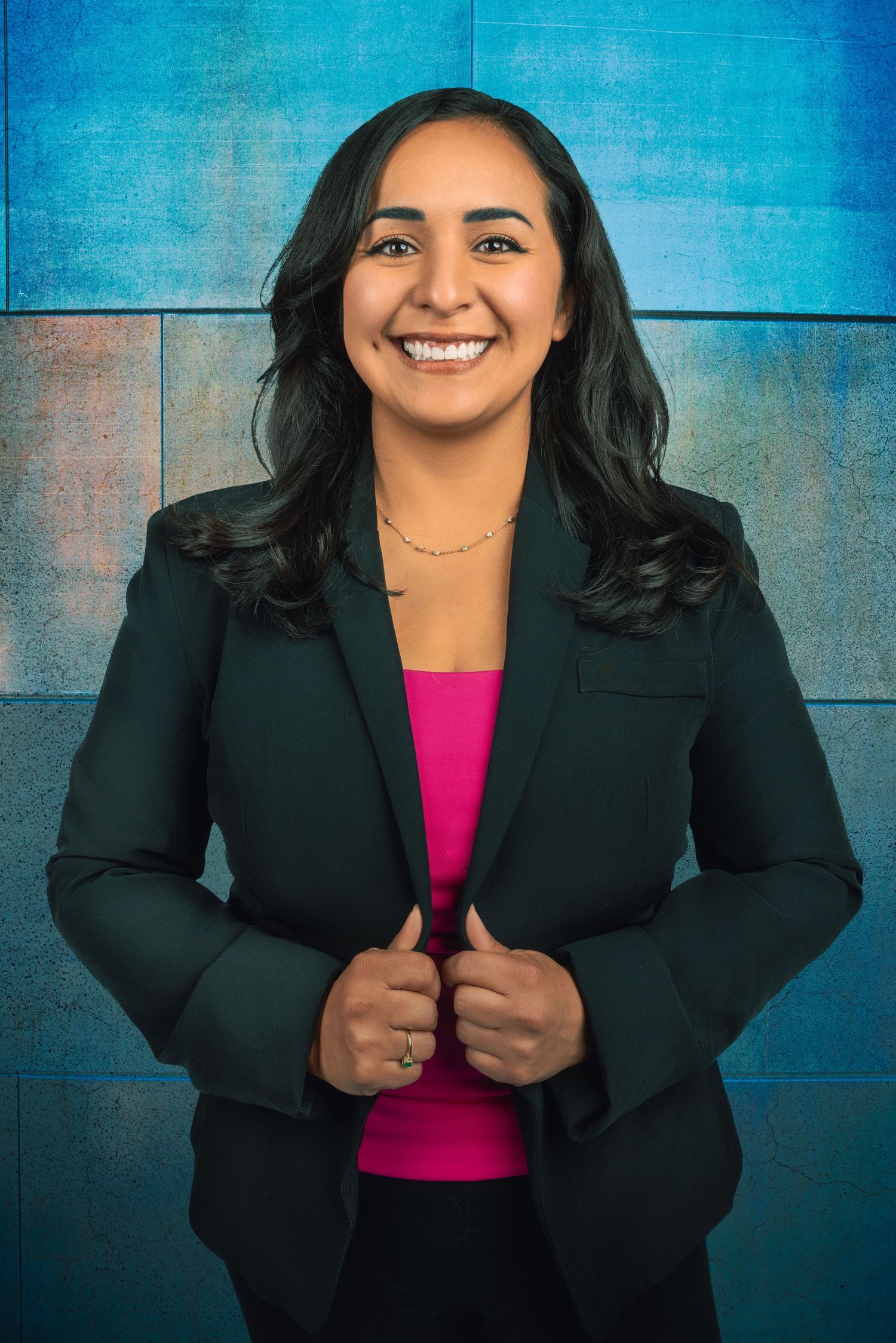 Professional portrait against blue textured wall wearing business attire.