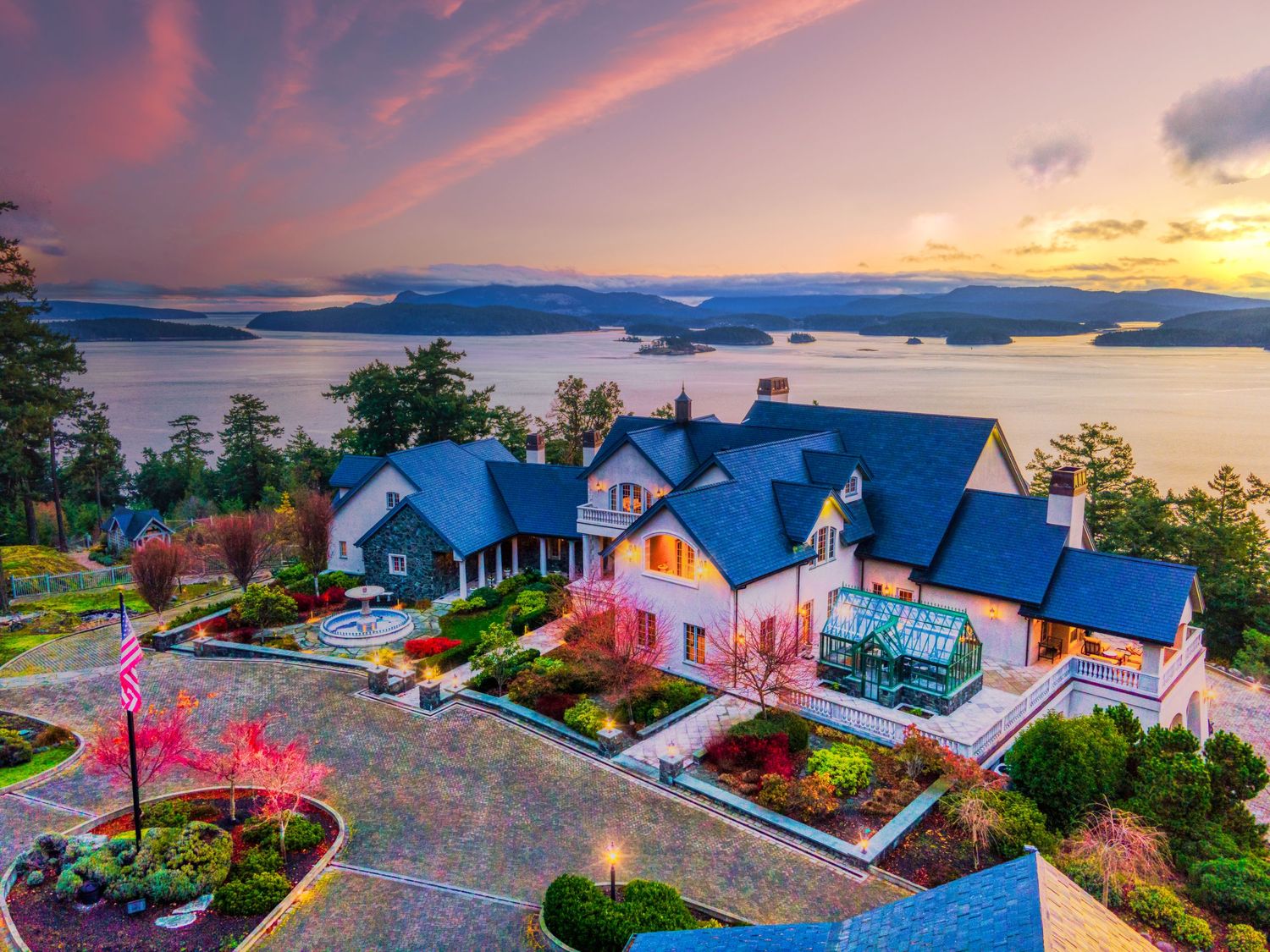 Luxury waterfront estate with pink sunset sky and manicured gardens overlooking mountain lake views.