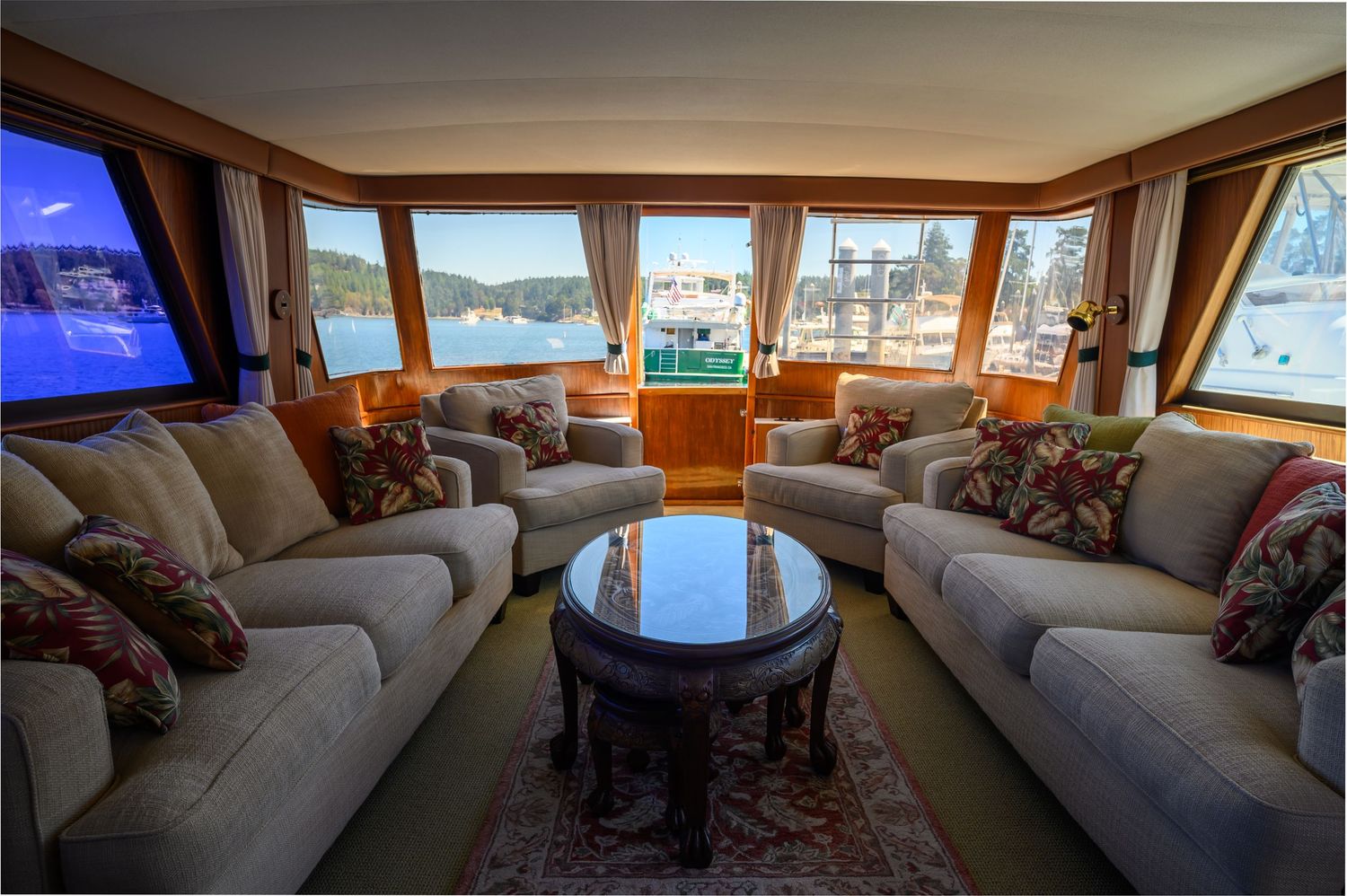 Luxurious yacht interior lounge with panoramic windows and plush beige sofas facing a water view.