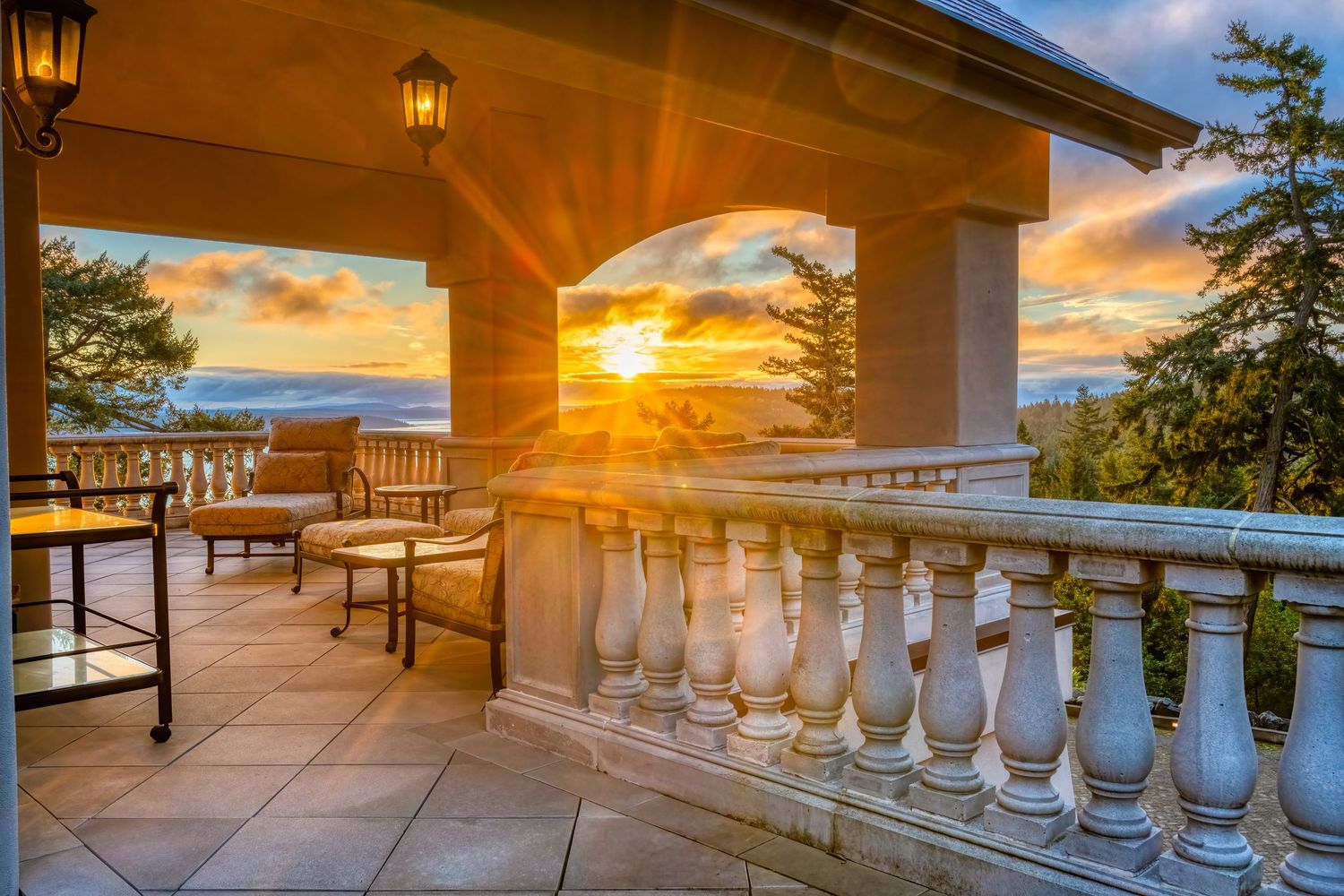 Elegant covered patio with white balustrades and wooden furniture capturing a dramatic ocean sunset.