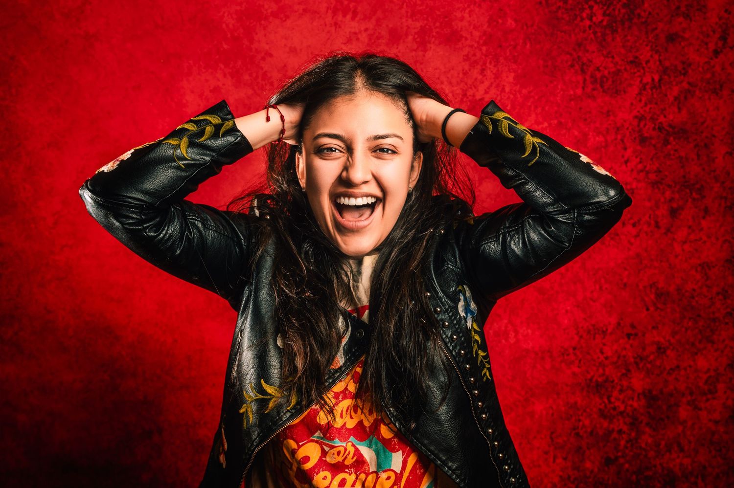 Person in black leather jacket expressing excitement against vibrant red background.