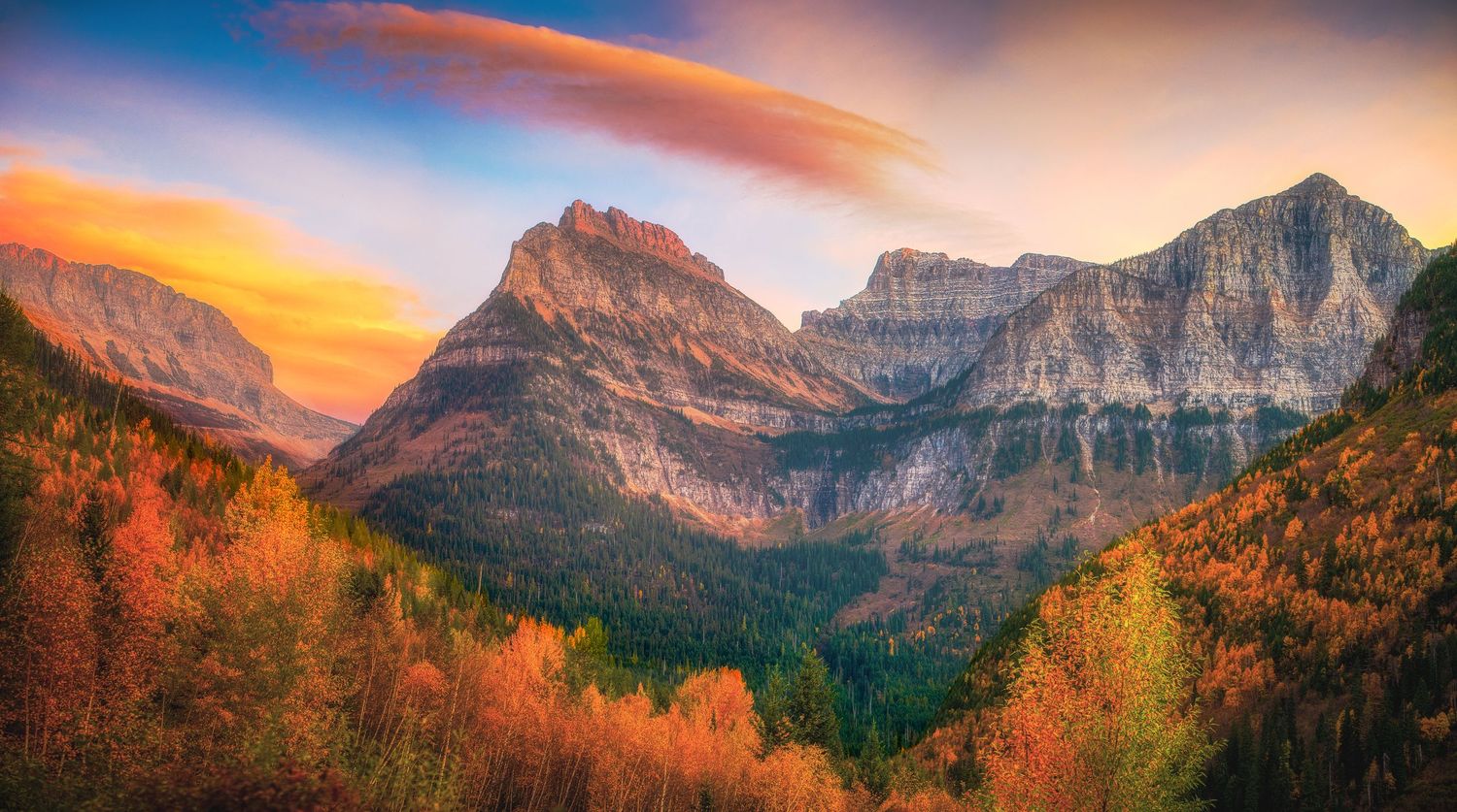 Dramatic mountain peaks glow orange during sunset in autumn with colorful fall foliage in foreground.
