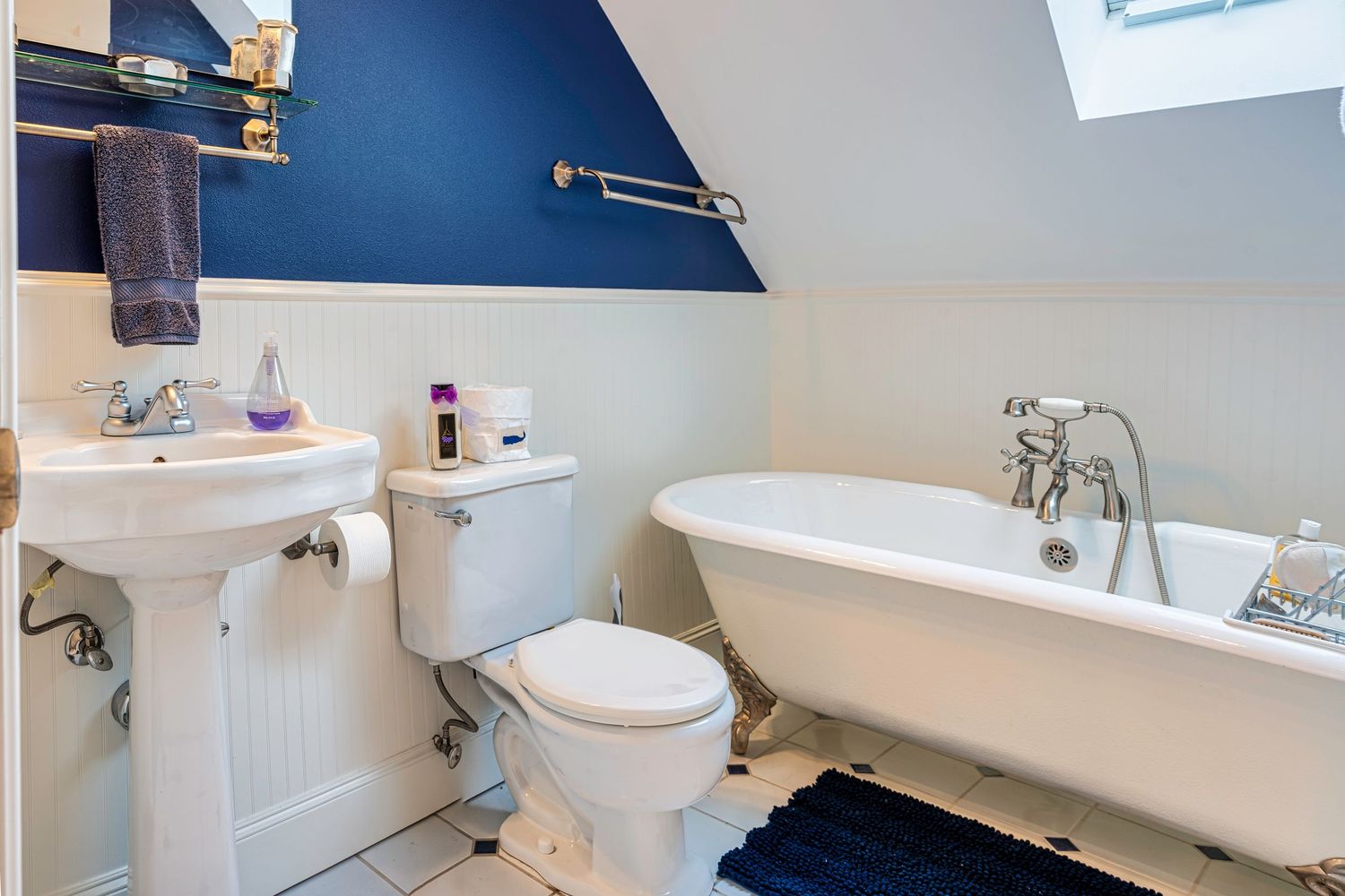 Classic bathroom with clawfoot tub, navy blue accent wall, and white pedestal sink.