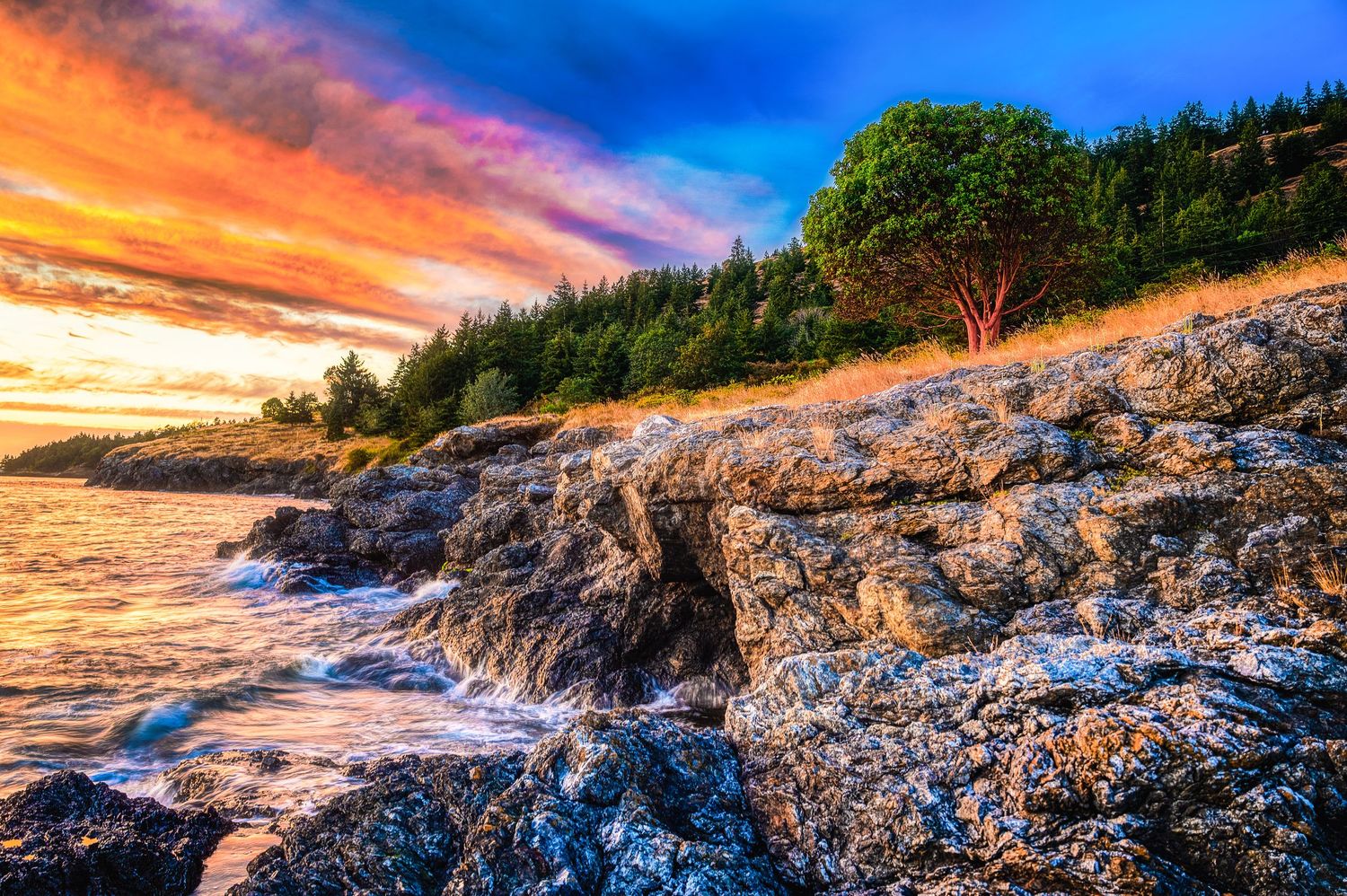 Dramatic sunset illuminates rocky coastal cliffs with orange and blue sky reflections.