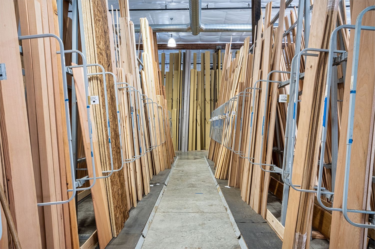Long corridor lined with wooden lumber and building materials in warehouse setting.