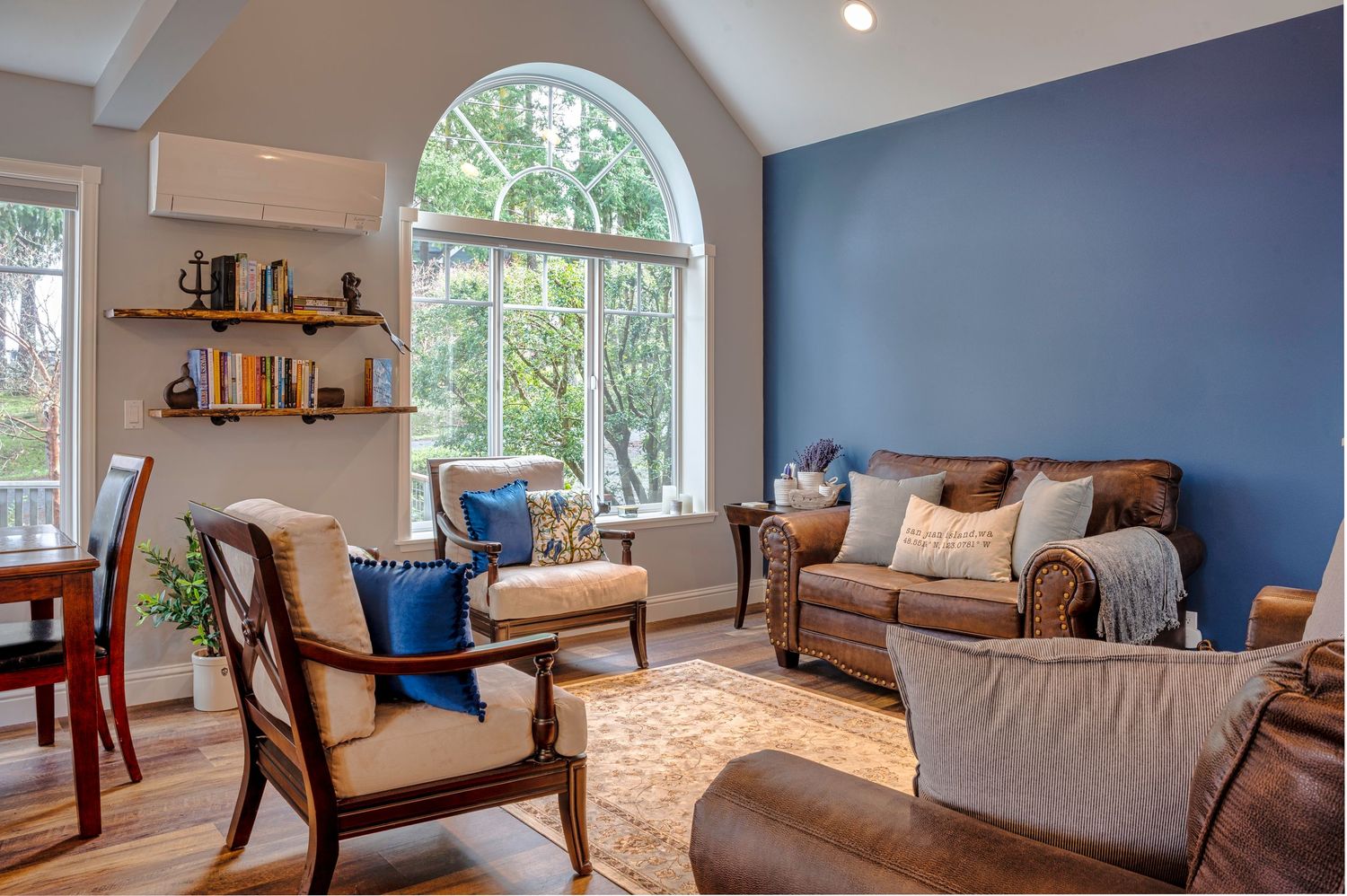 Cozy living room with arched window, blue accent wall, and comfortable brown furniture.