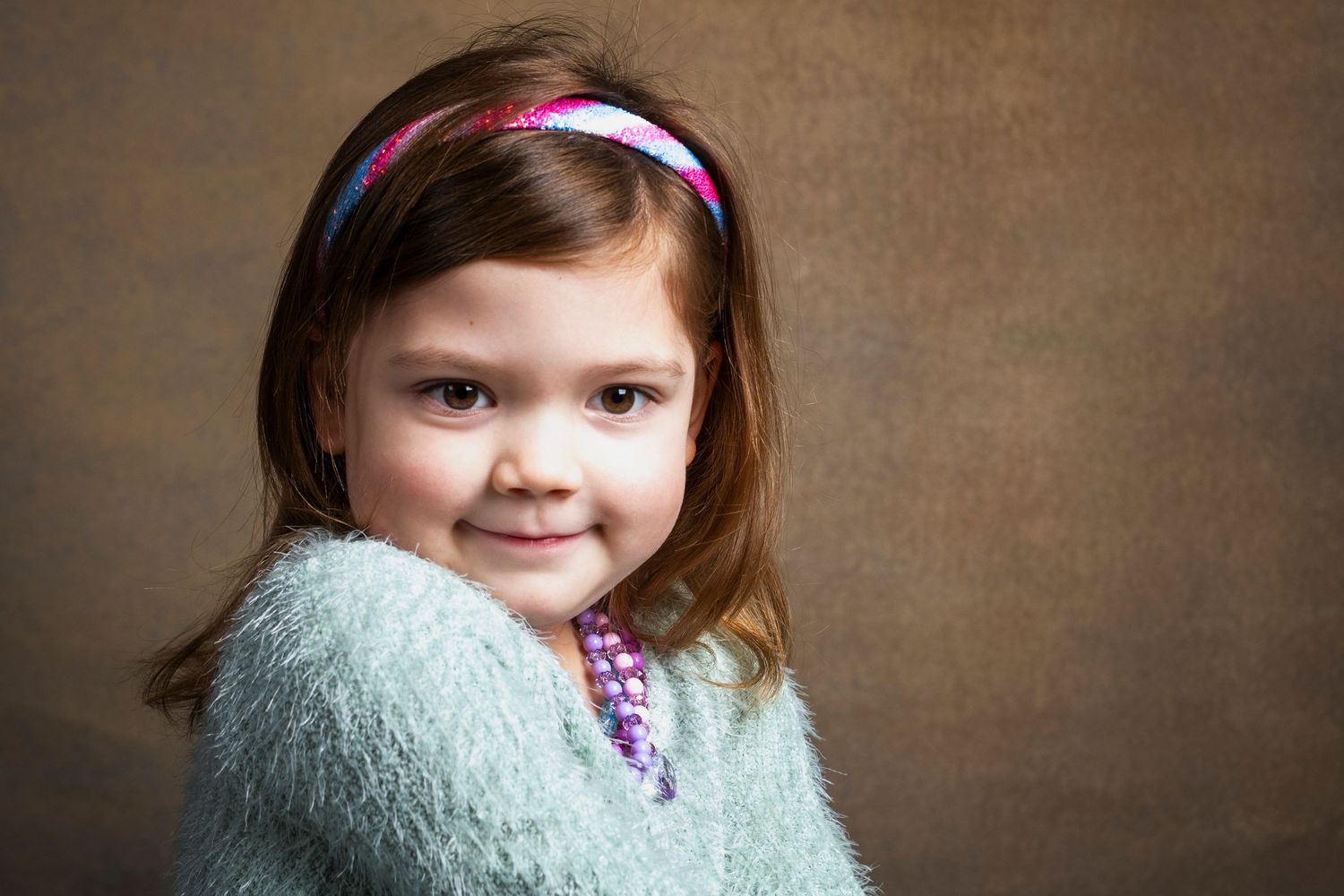 Studio portrait of a young child wearing a fuzzy white sweater and pink headband.
