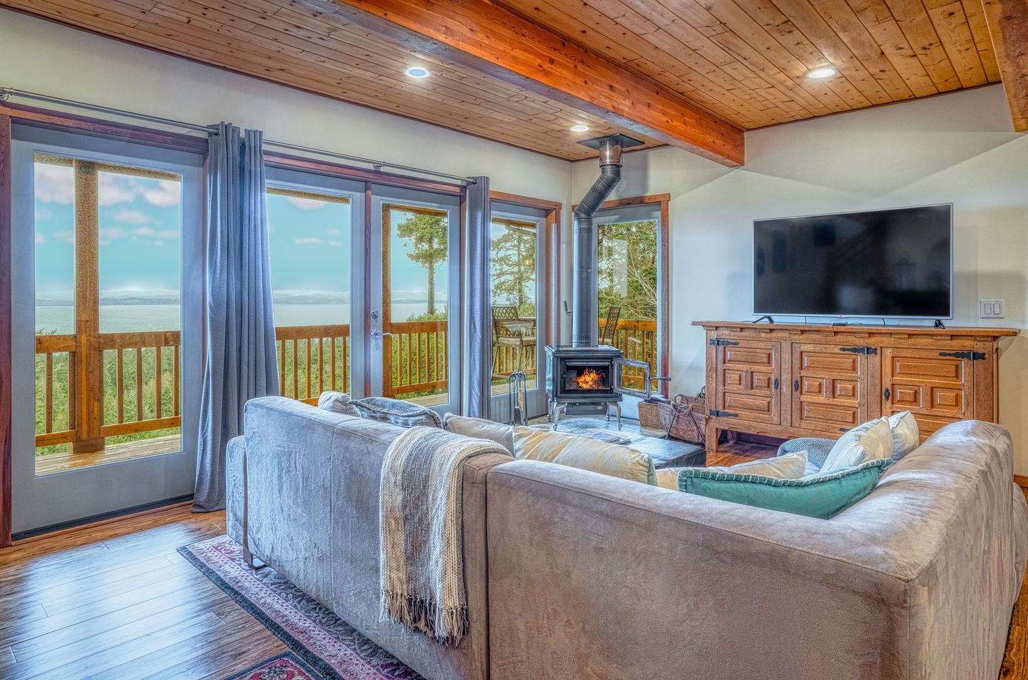 Contemporary living room with vaulted wood ceiling, grey sectional, and panoramic windows overlooking mountain views.