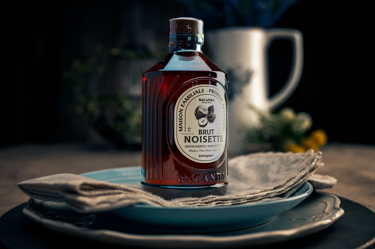 Artisanal maple syrup bottle on vintage plates with dark moody lighting and rustic styling.