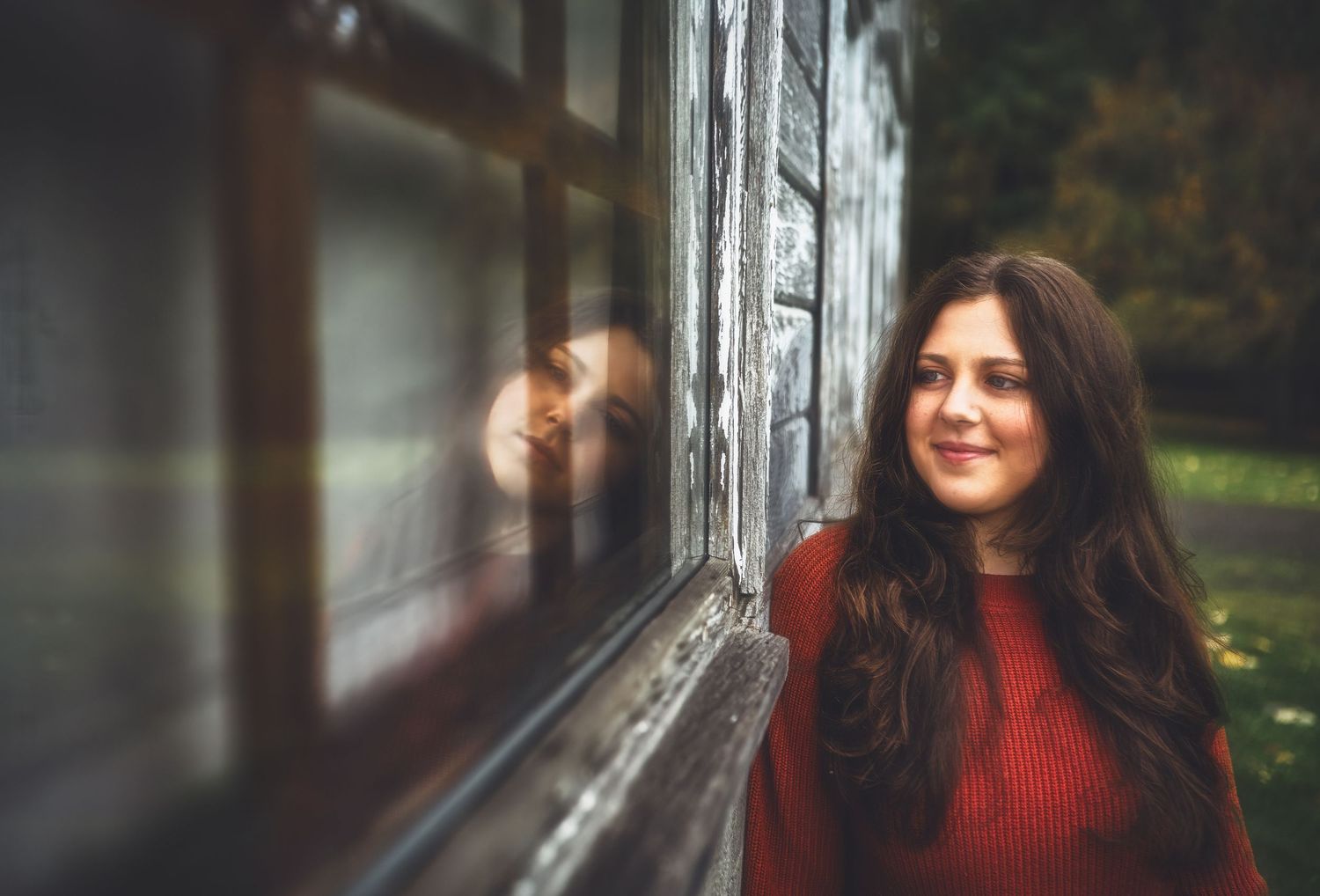 Artistic portrait by a window wearing a red sweater with soft natural lighting.