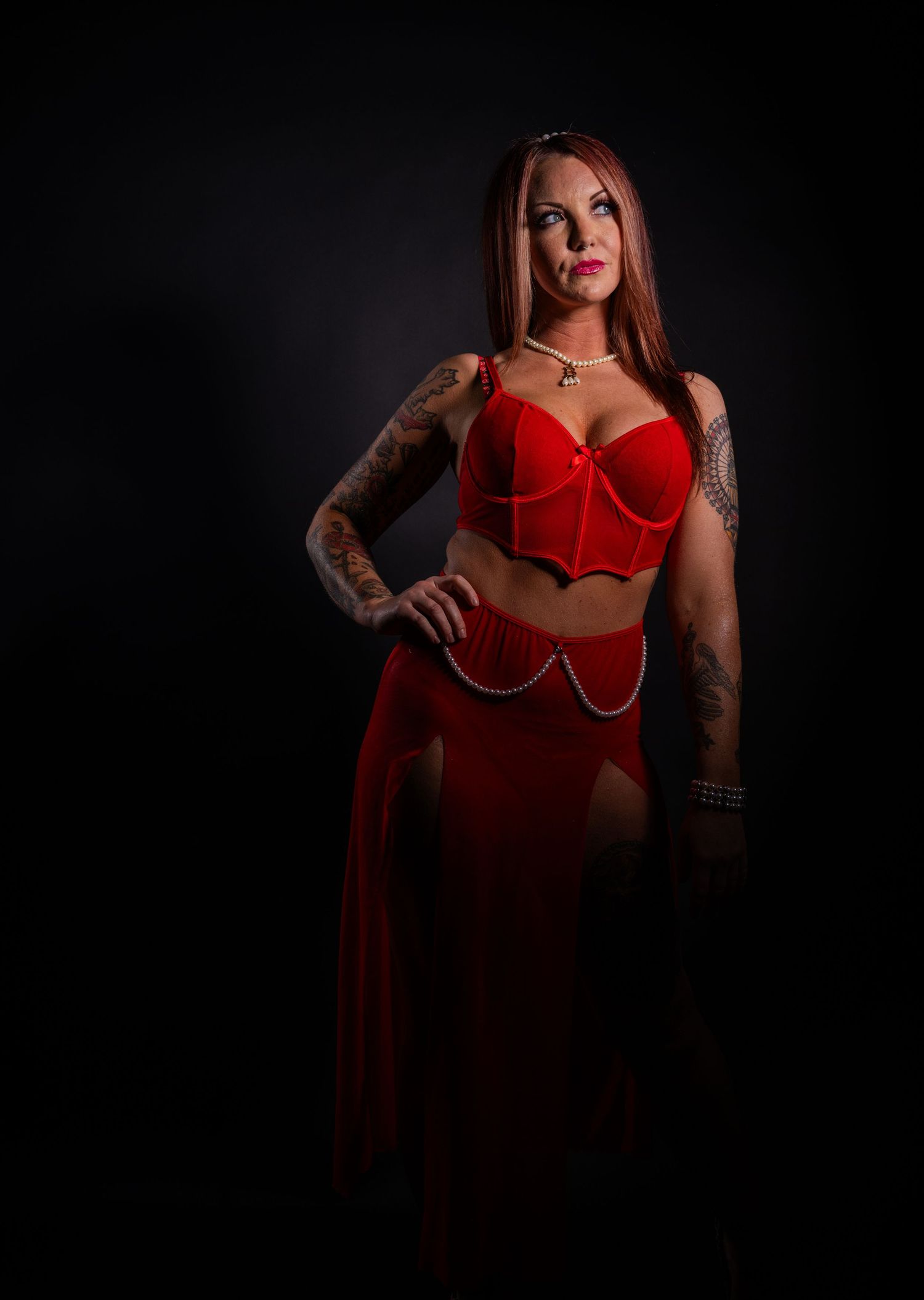 Dark and moody portrait in red costume with chain details and tattoos.