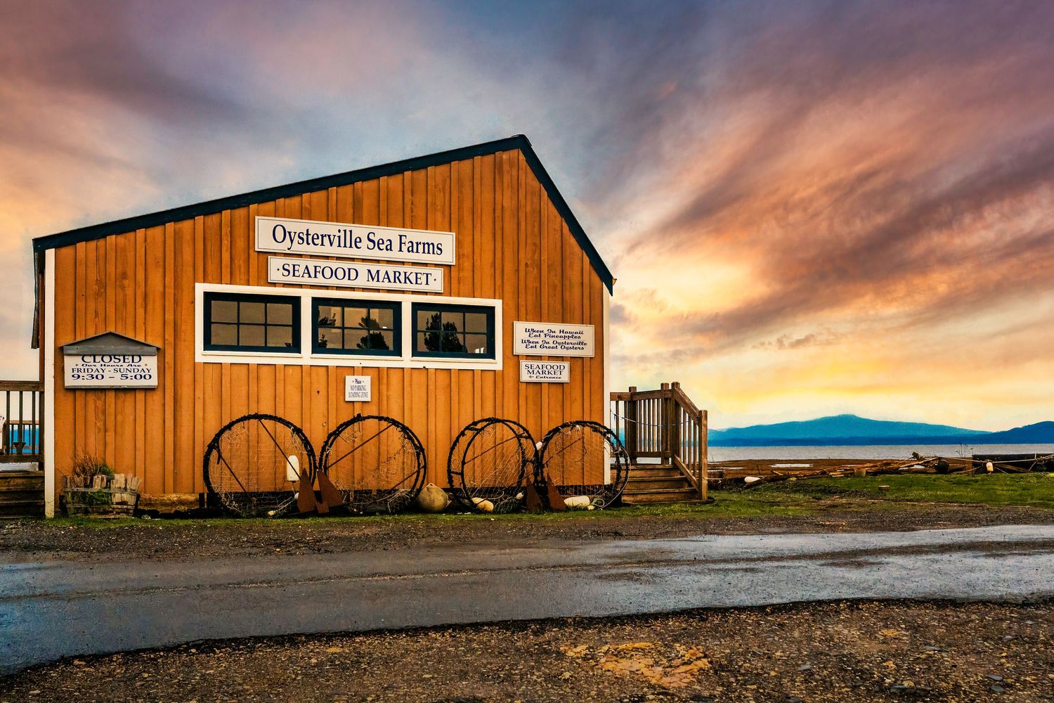 Rustic wooden building with wagon wheels at sunset features dramatic orange and purple sky in rural setting.