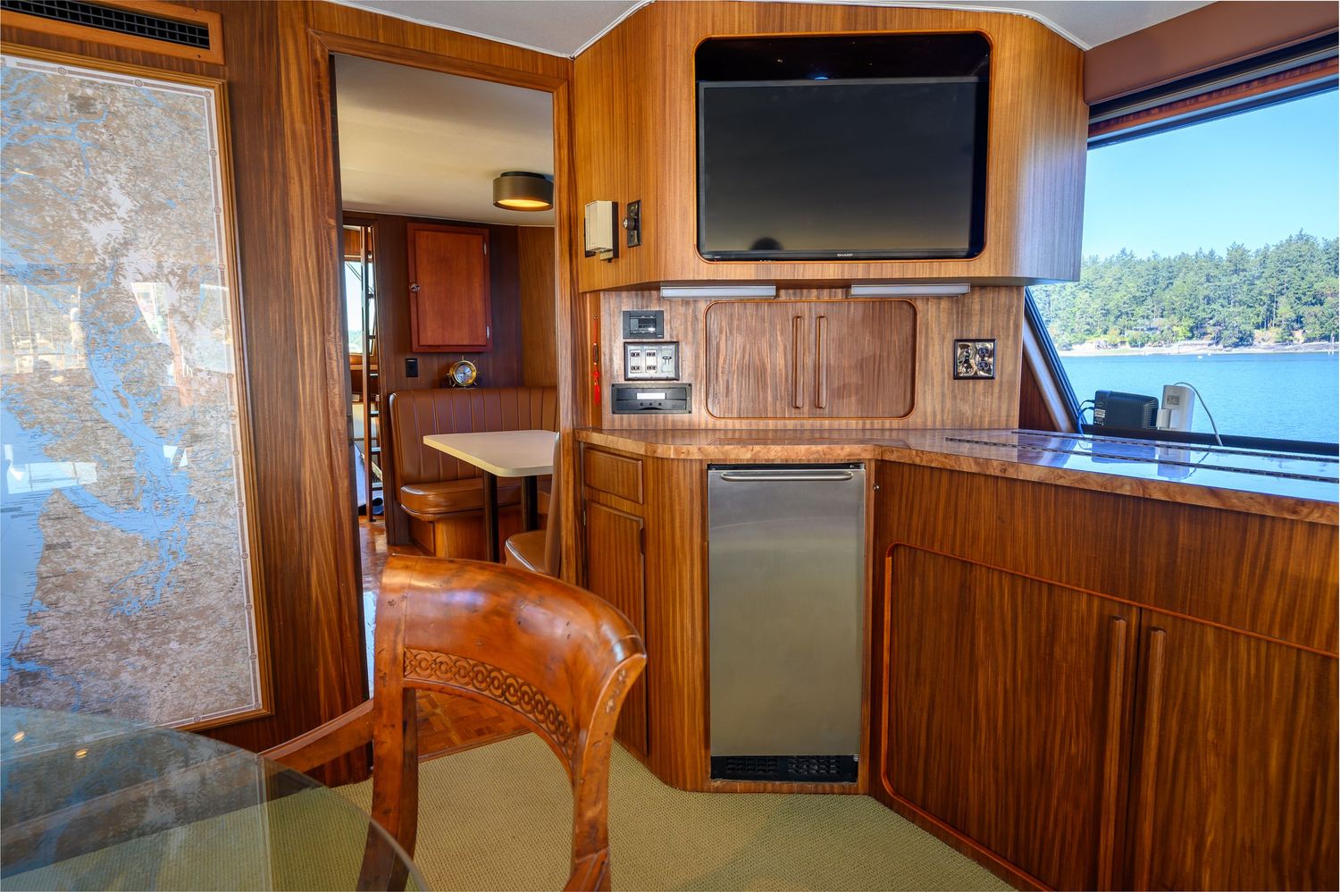 Modern yacht galley featuring wood paneling, mounted TV, and mini fridge in a compact corner setup.