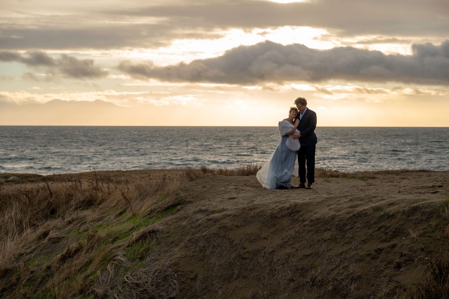 Silhouettes against a dramatic sunset sky on a coastal cliff edge.