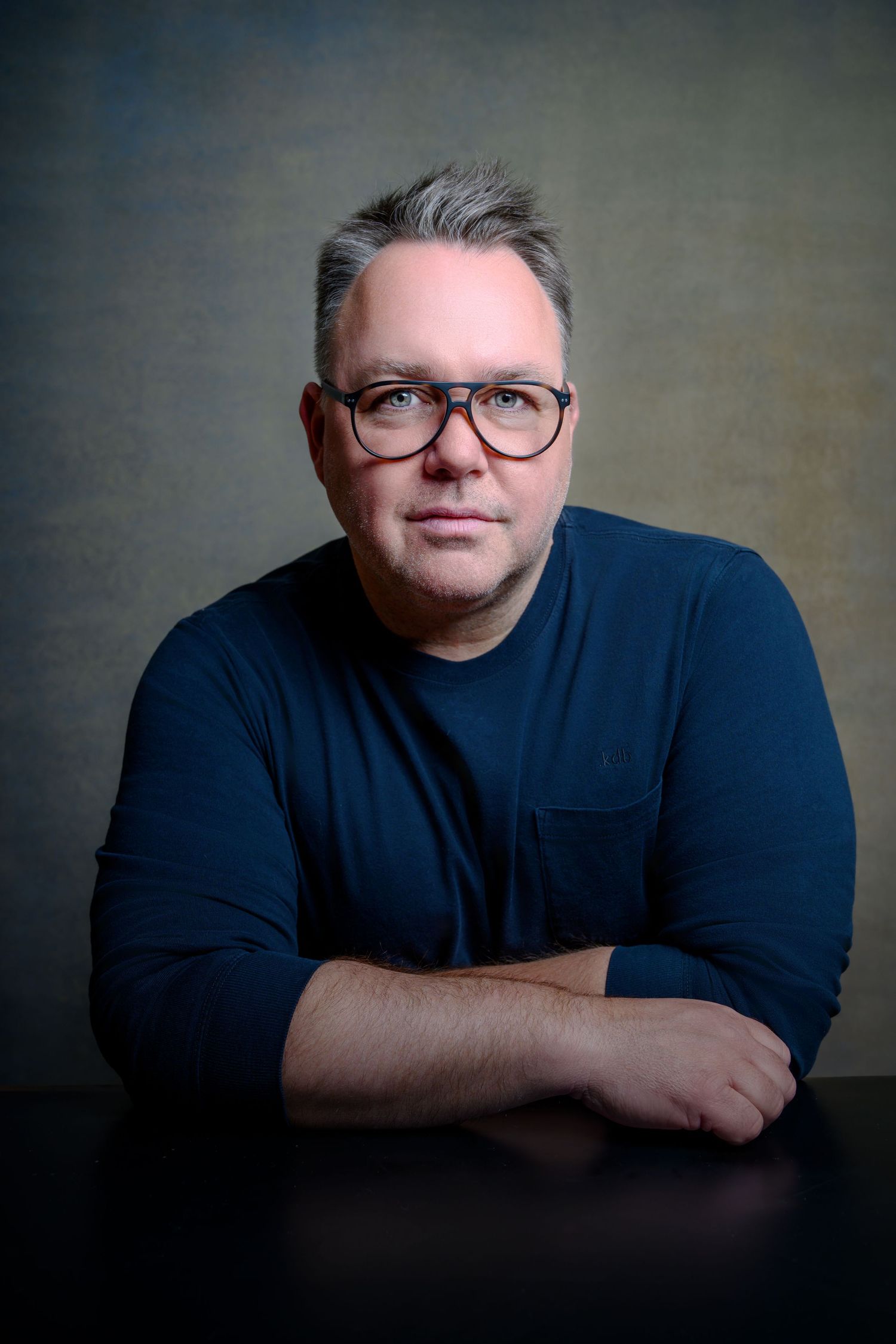 Professional headshot of person in navy sweater against dark background with studio lighting.