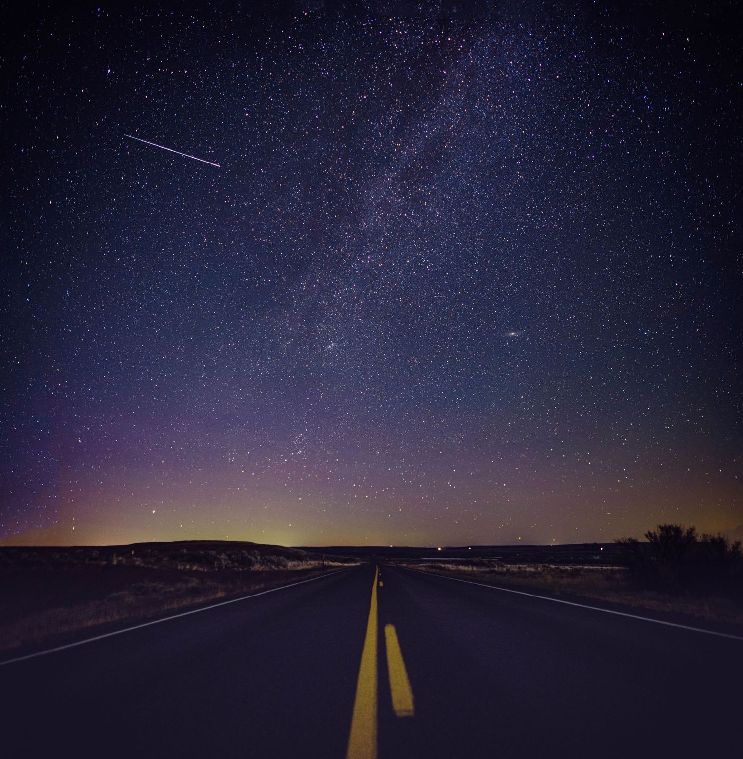 Empty highway stretches towards starry night sky with vibrant Milky Way overhead.