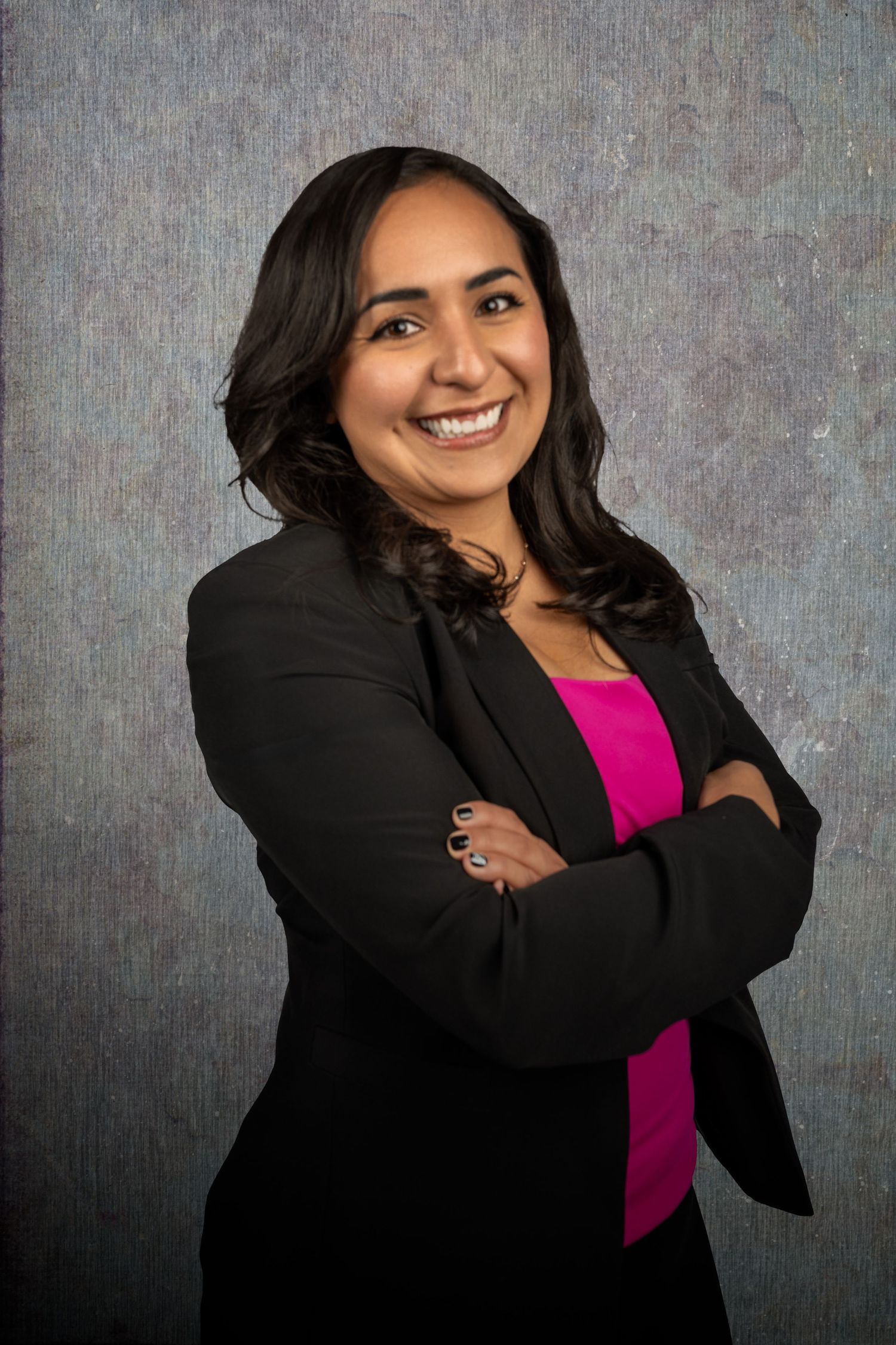 Business portrait of person in dark blazer and pink top against textured background.