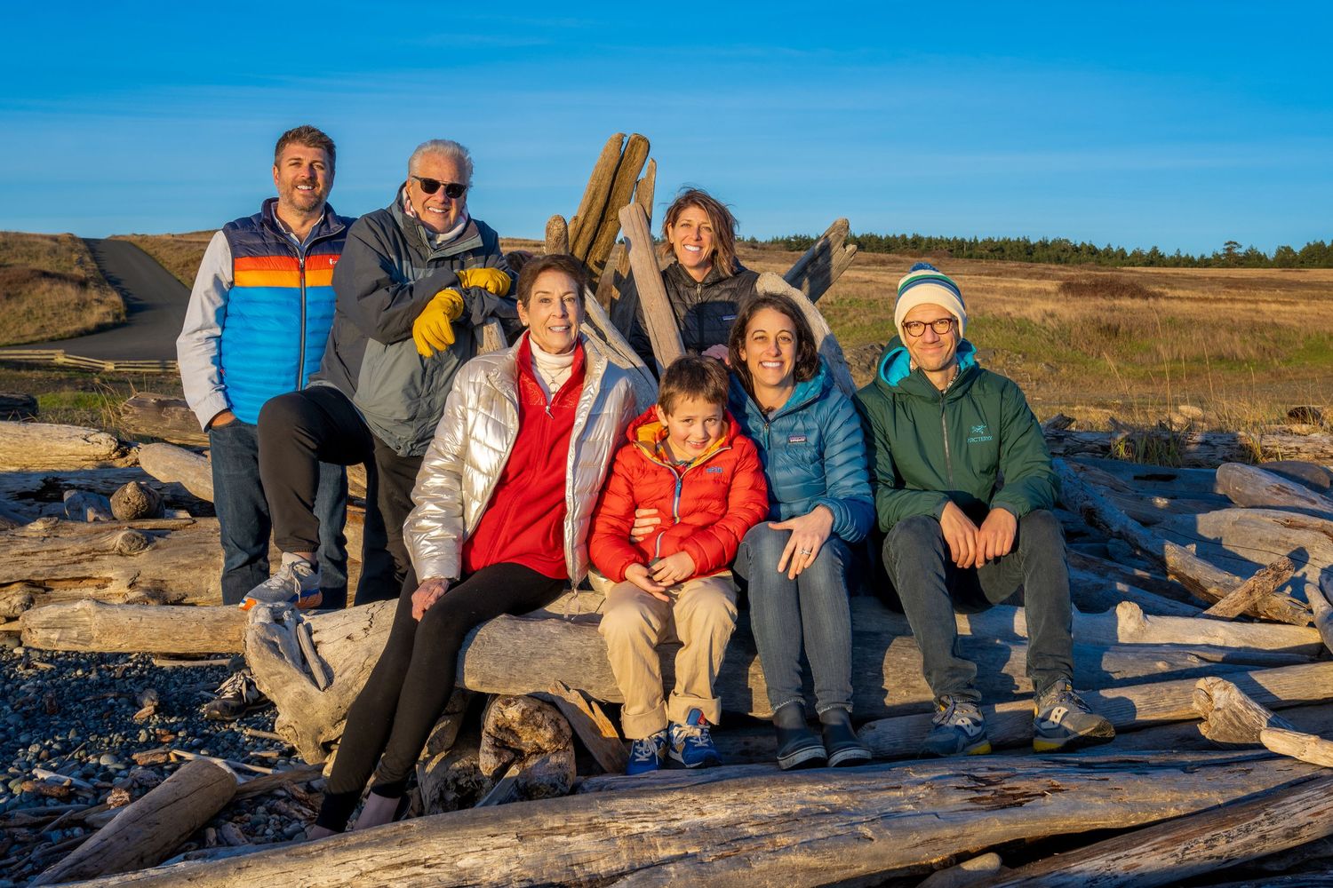 Family group sitting together on driftwood at the beach during golden hour.