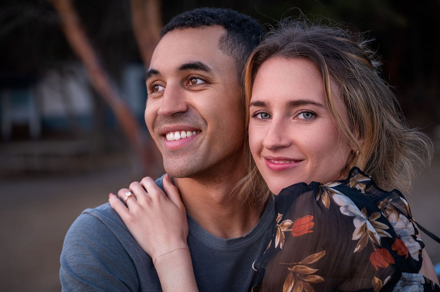 A romantic couple sitting close together outdoors during golden hour sharing an intimate moment.