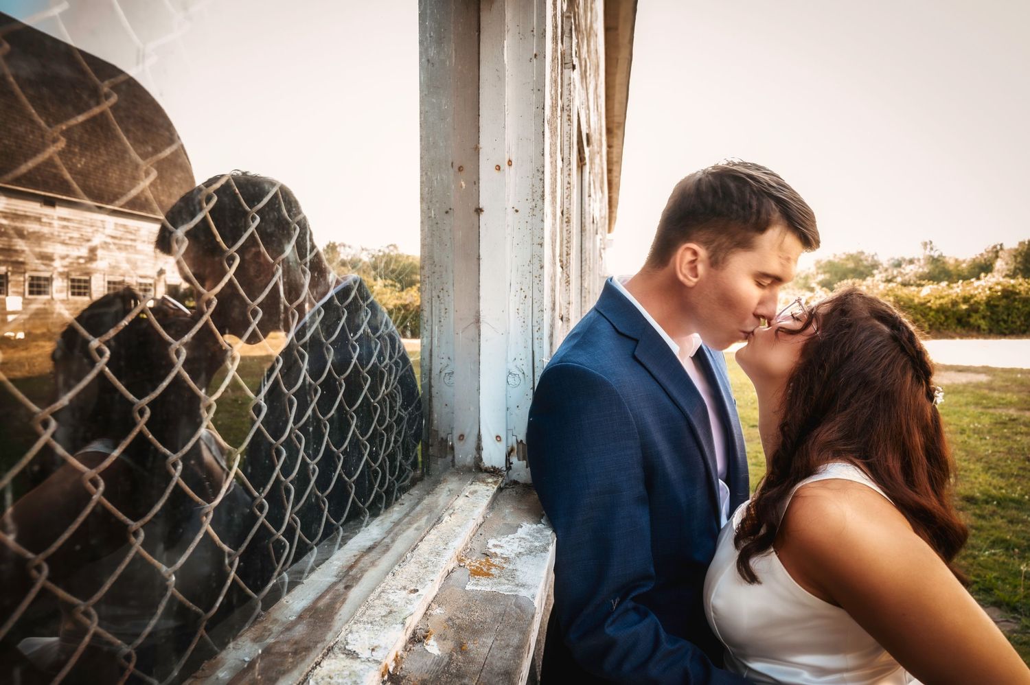 A romantic couple sharing an intimate moment against a rustic wall with wire fencing.