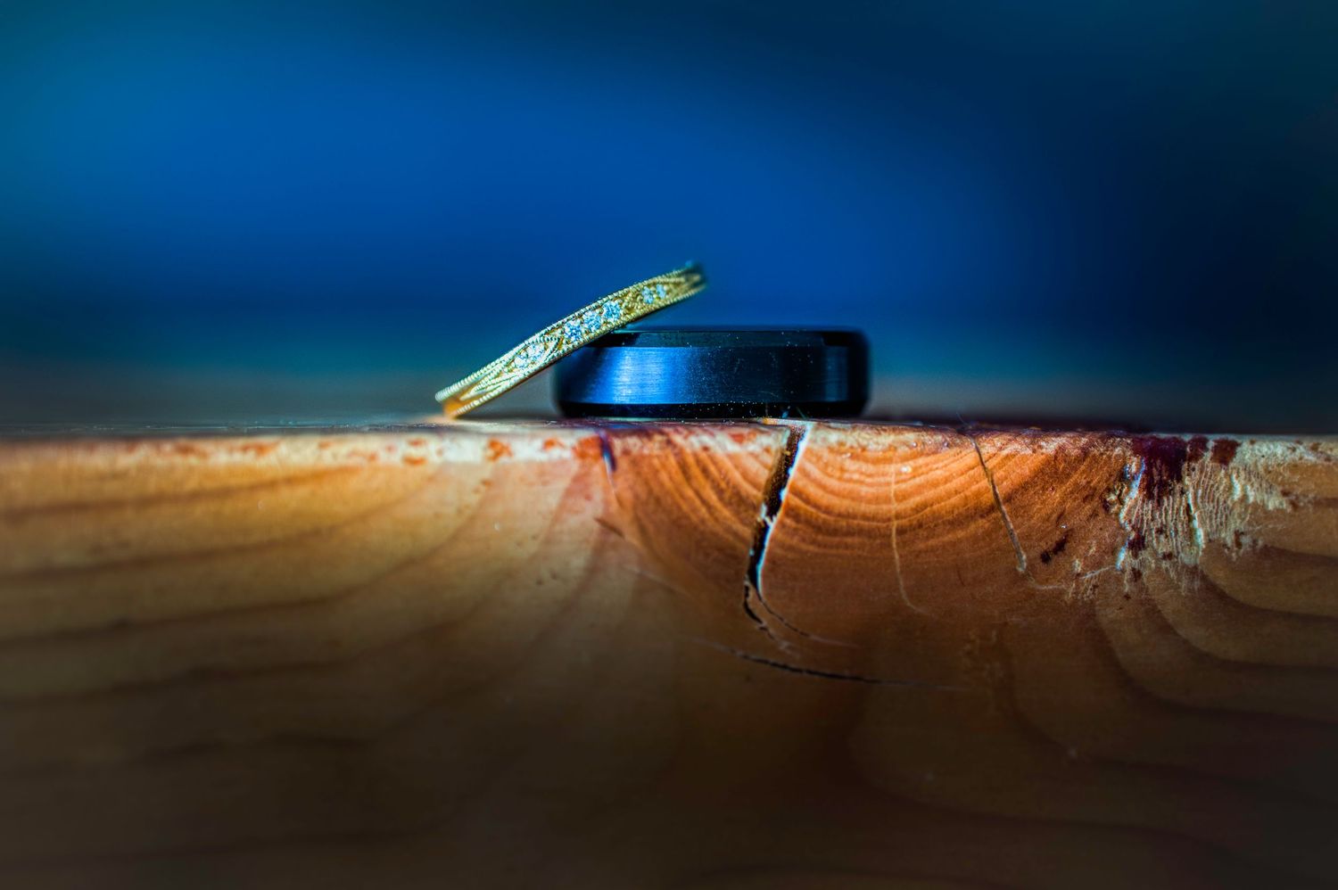 Wedding rings artistically photographed on wooden surface with blue background lighting.