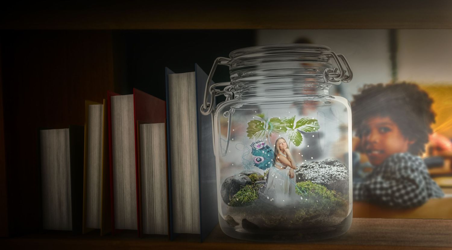 Glass jar with whimsical fairy garden design next to a row of books.