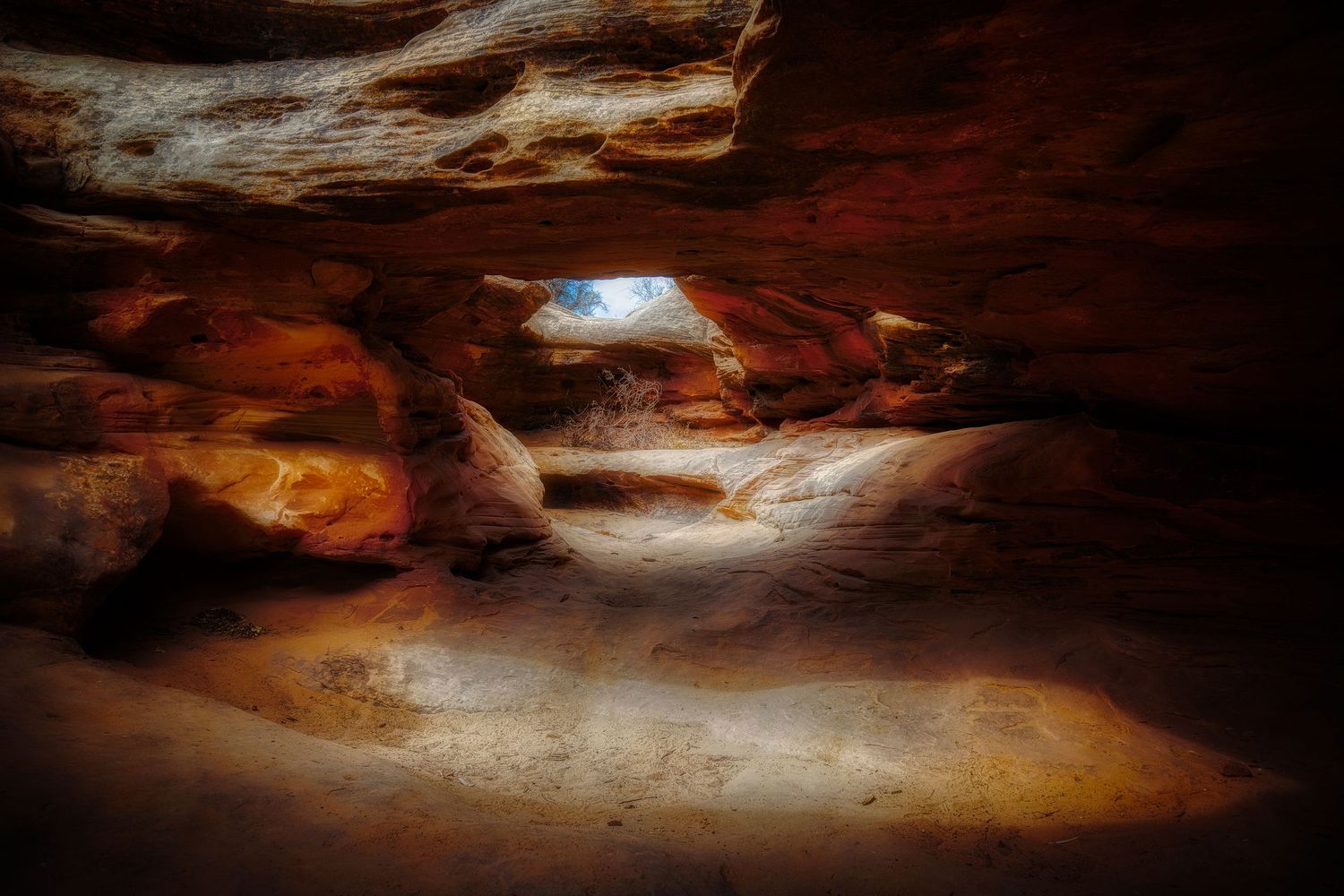 Natural light streams through a hole in the ceiling of a red sandstone cave formation.