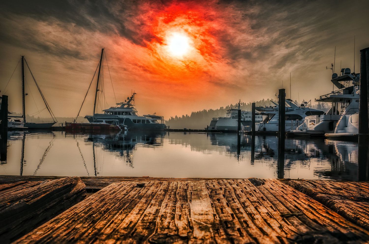 Boats dock at a misty marina under an intense red sun and dramatic cloudy sky.