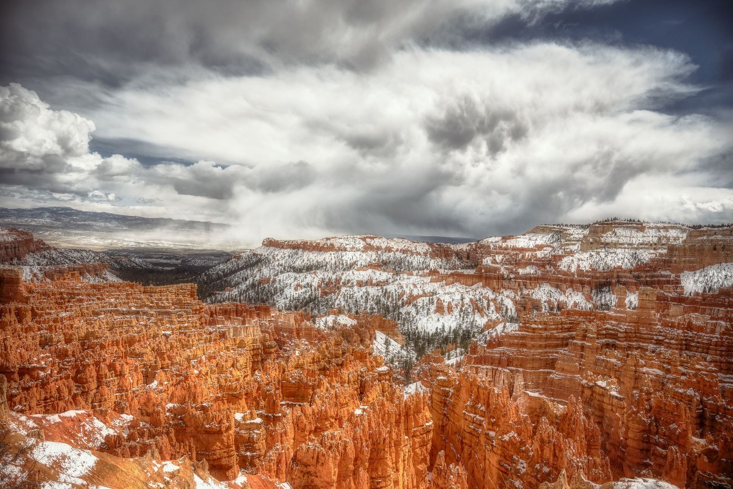 Aerial view of snow-dusted Bryce Canyon amphitheater under dramatic cloudy skies.
