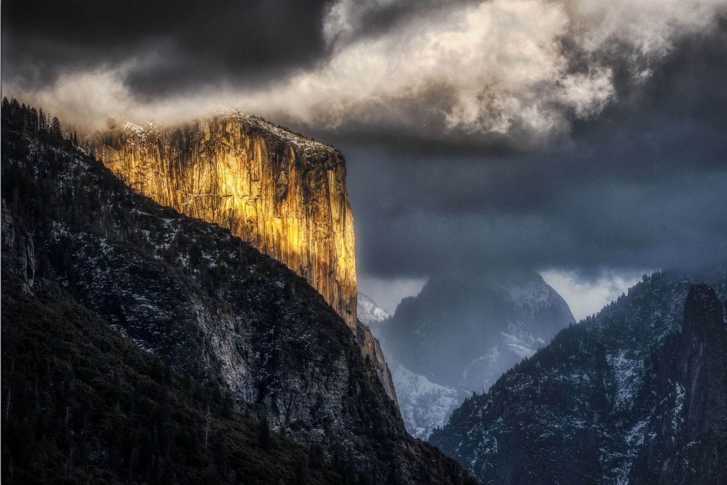 Sunlight illuminates El Capitan's face in Yosemite Valley as storm clouds gather overhead.