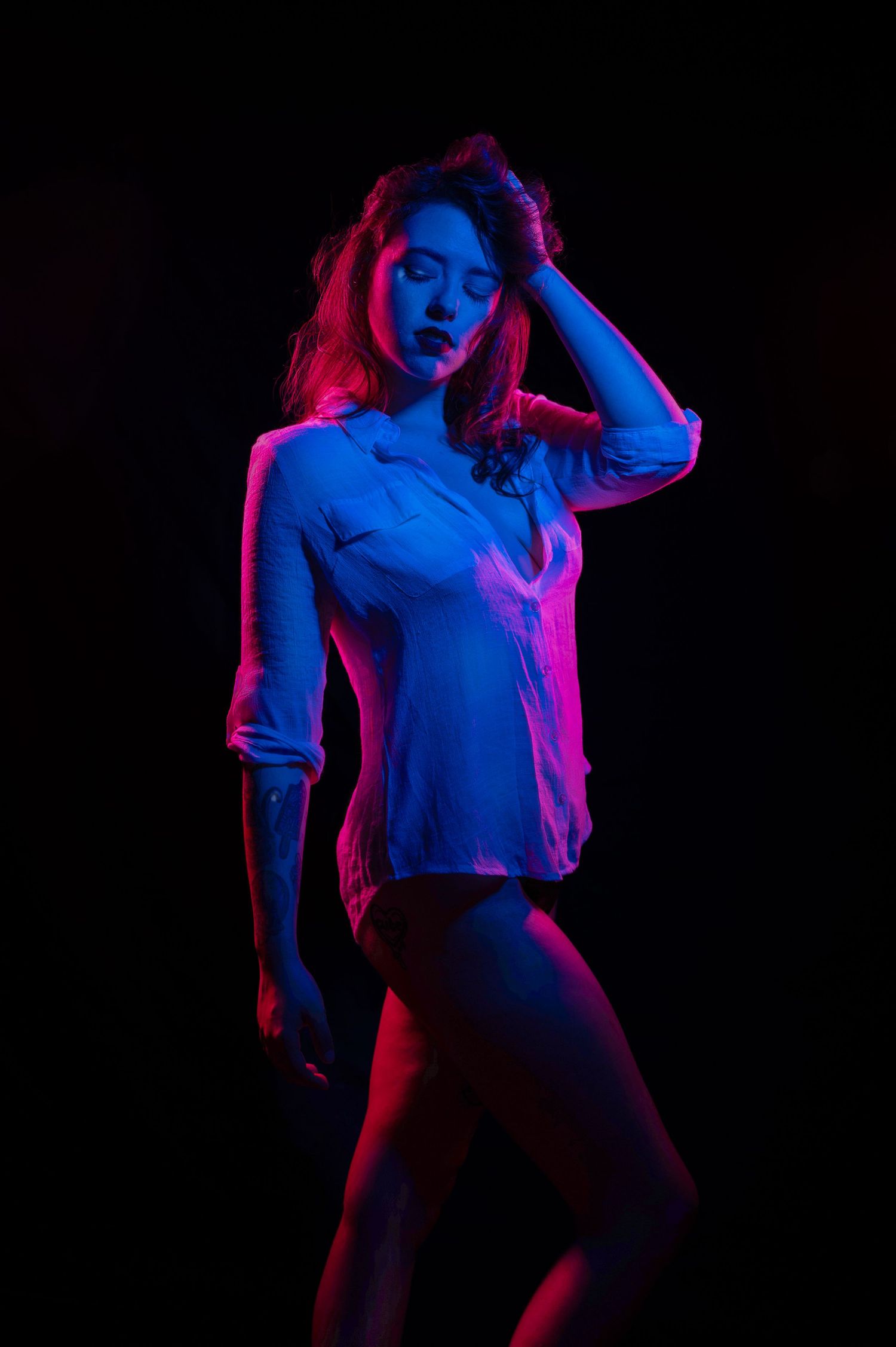 Dramatic portrait with red and blue neon lighting against dark background.