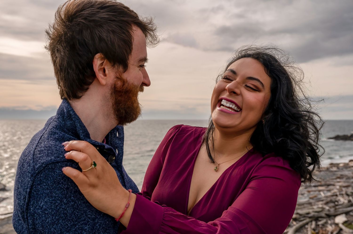 Couple laughing together by the ocean during sunset.