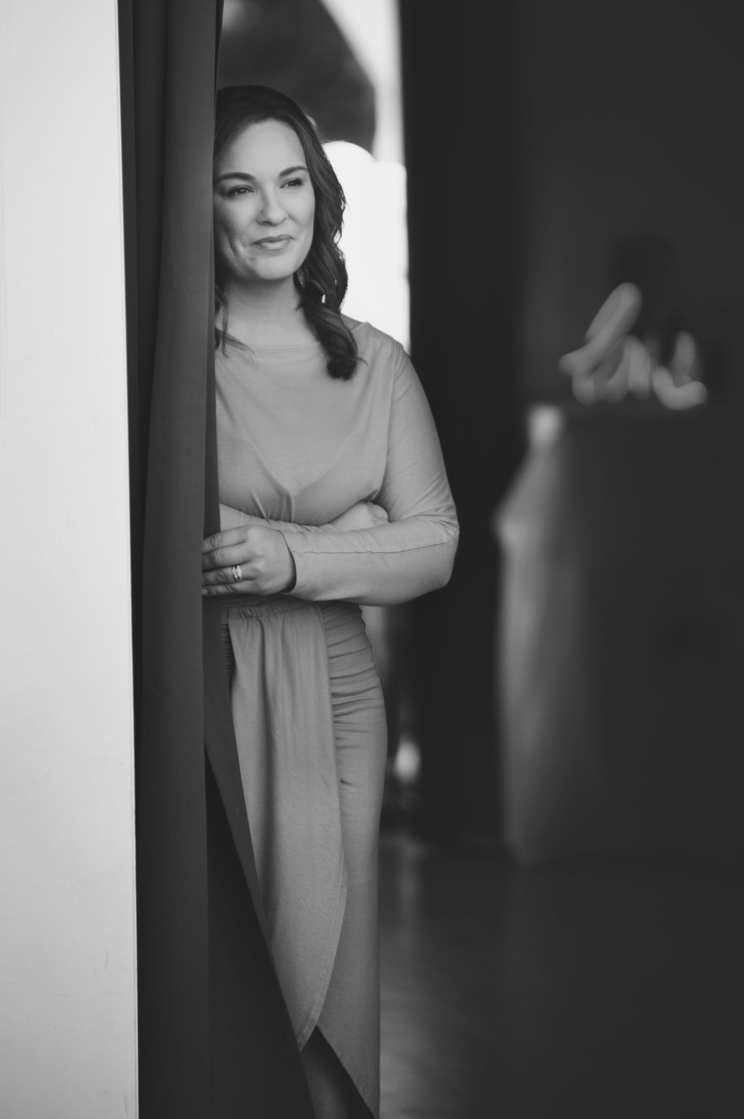 Black and white portrait of someone in formal dress standing in a doorway with dramatic lighting.