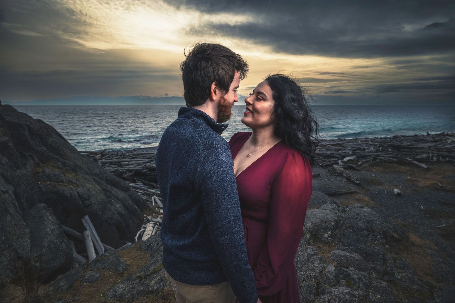 Romantic couple embraces on rocky coastal cliffs at sunset.