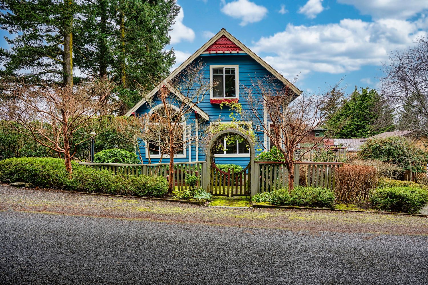 Charming blue cottage with white trim and picket fence surrounded by garden landscaping.