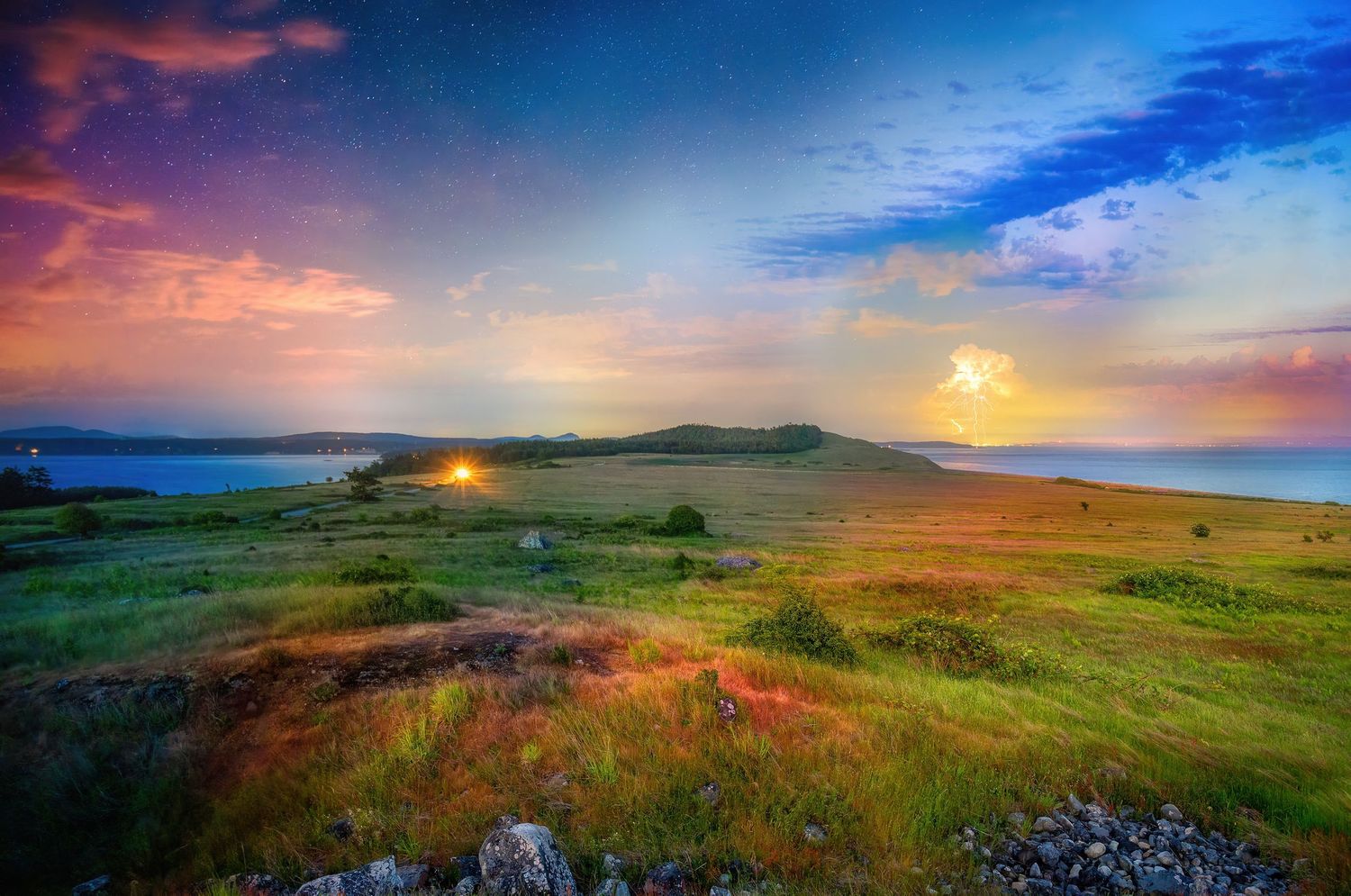 Rolling green hills under colorful sunrise sky with distant mountains and ocean view.