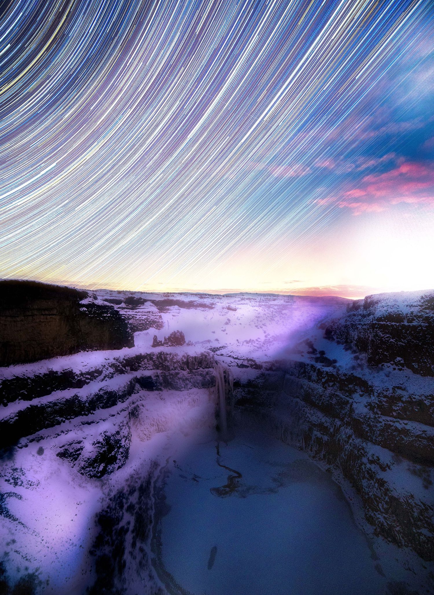 Star trails sweep across a purple twilight sky above a snowy canyon landscape.