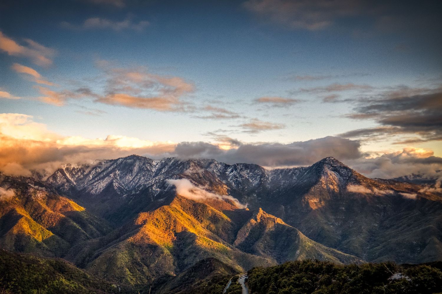 Dramatic sunset illuminates snow-capped mountain peaks against a cloudy sky.