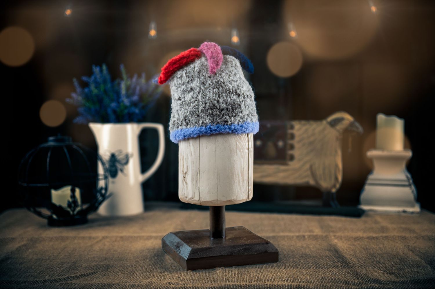 Decorative winter hat on display stand with festive bokeh lights and home decor in background.
