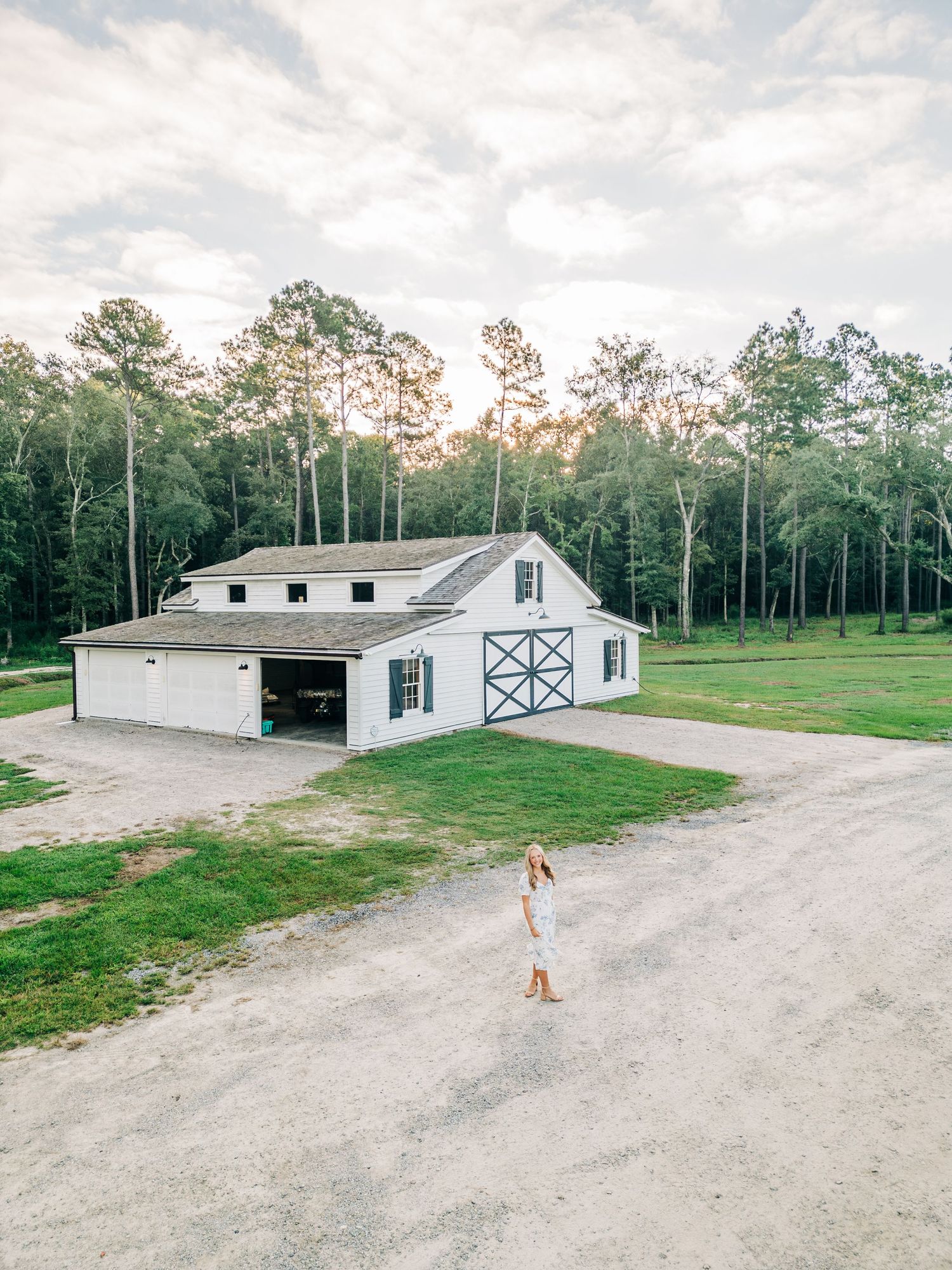 Modern white barn-style building with black trim surrounded by trees at sunset.