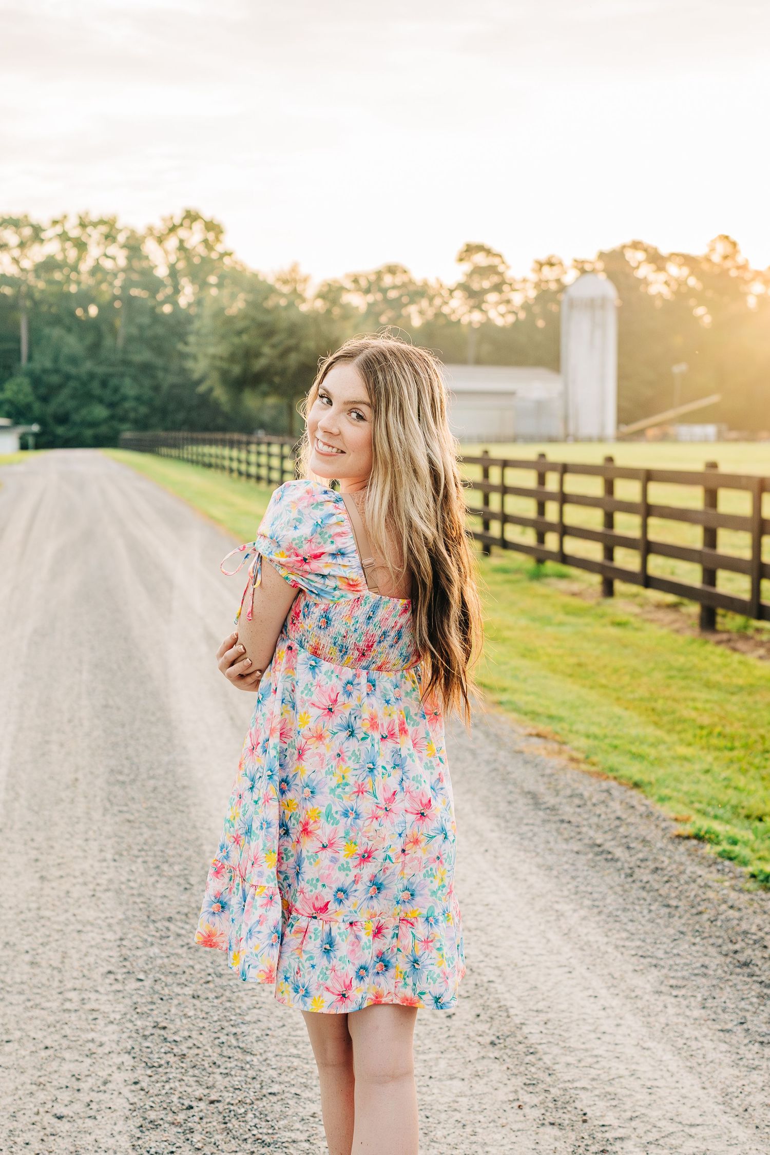 A floral print dress photographed on a rustic country road with fenced pastures at sunset.
