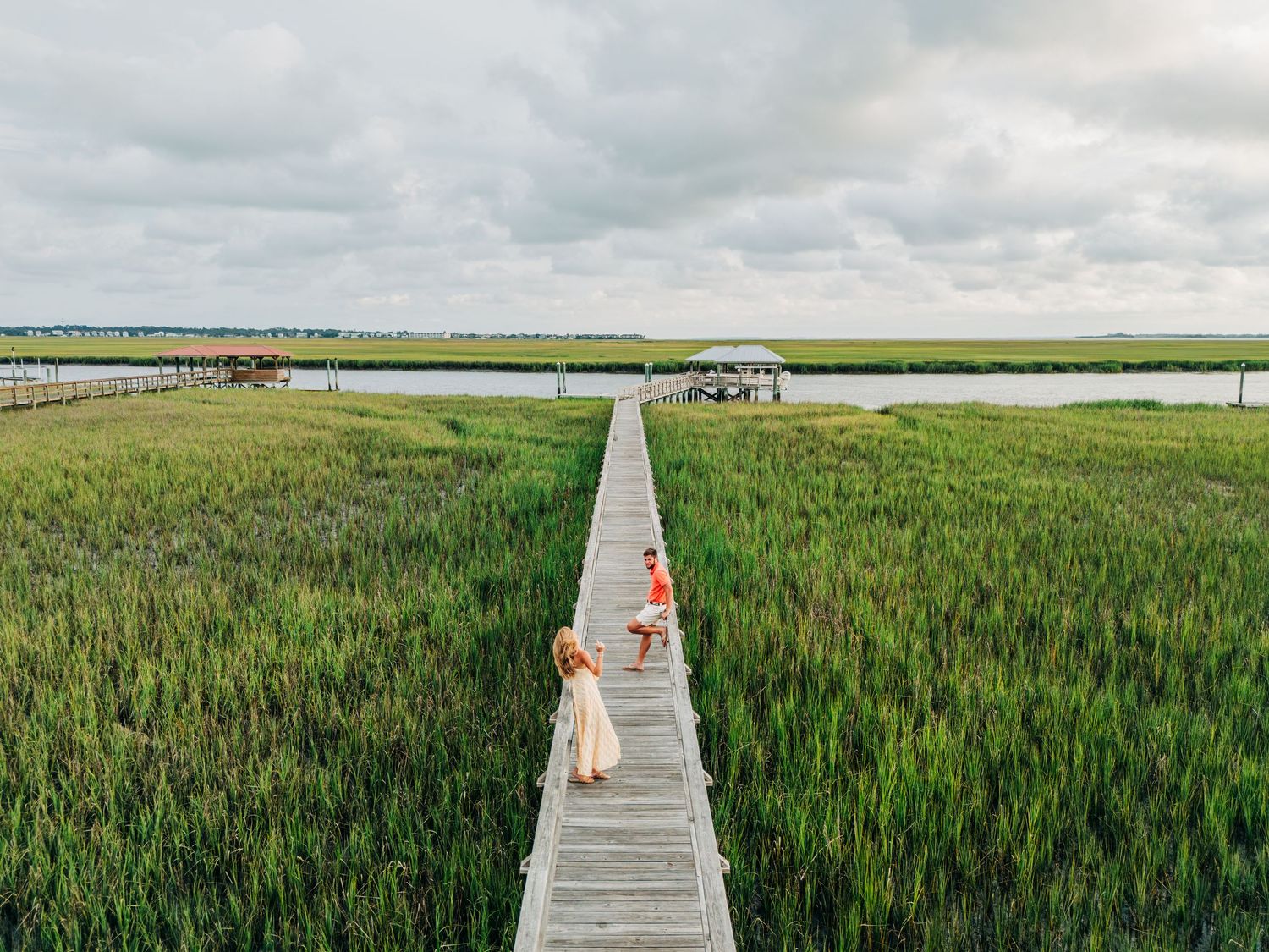 Wooden boardwalk extends across scenic coastal wetlands with salt marsh grasses and waterways under cloudy skies.