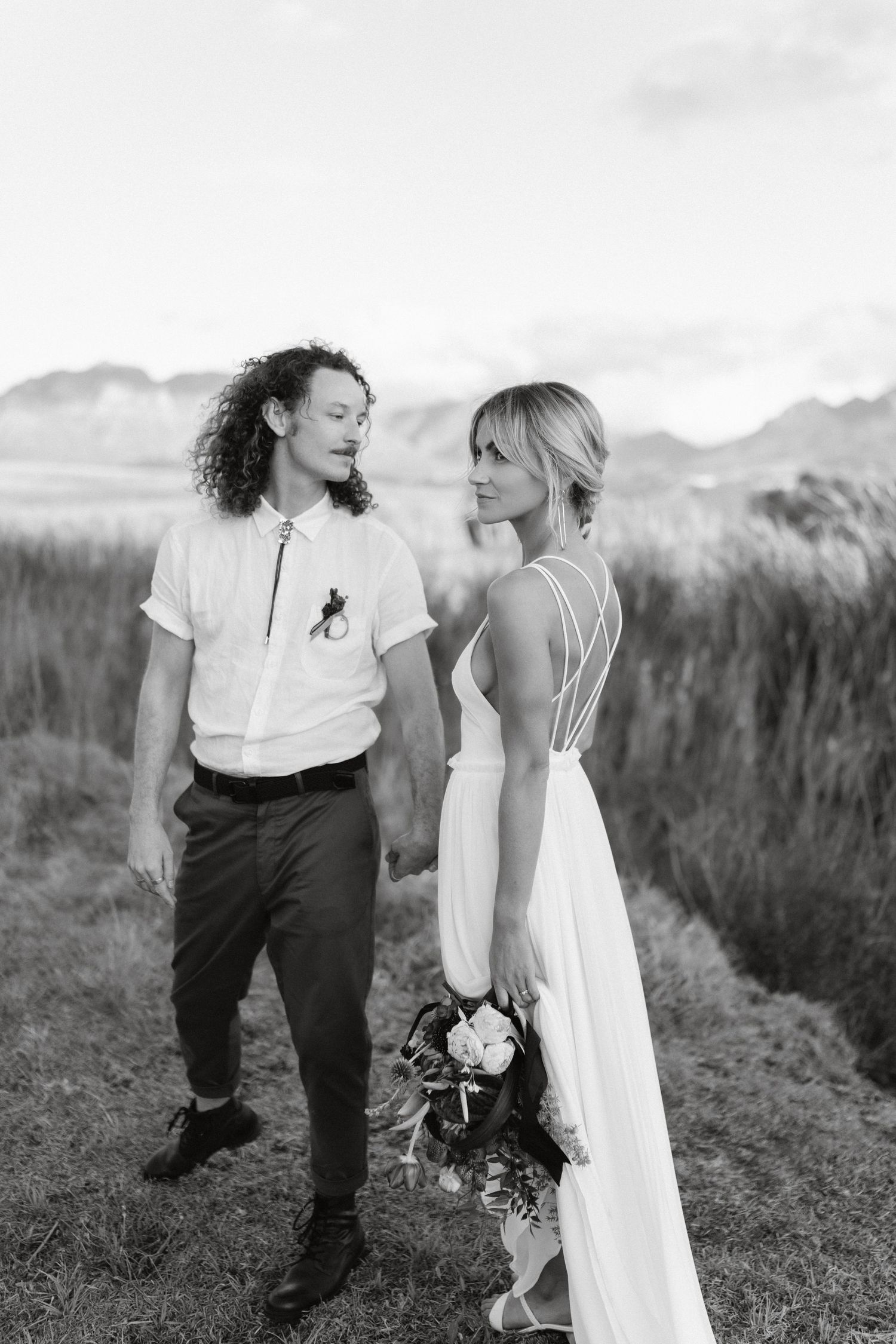 Black and white wedding photo of couple standing together on hillside with mountains in background.