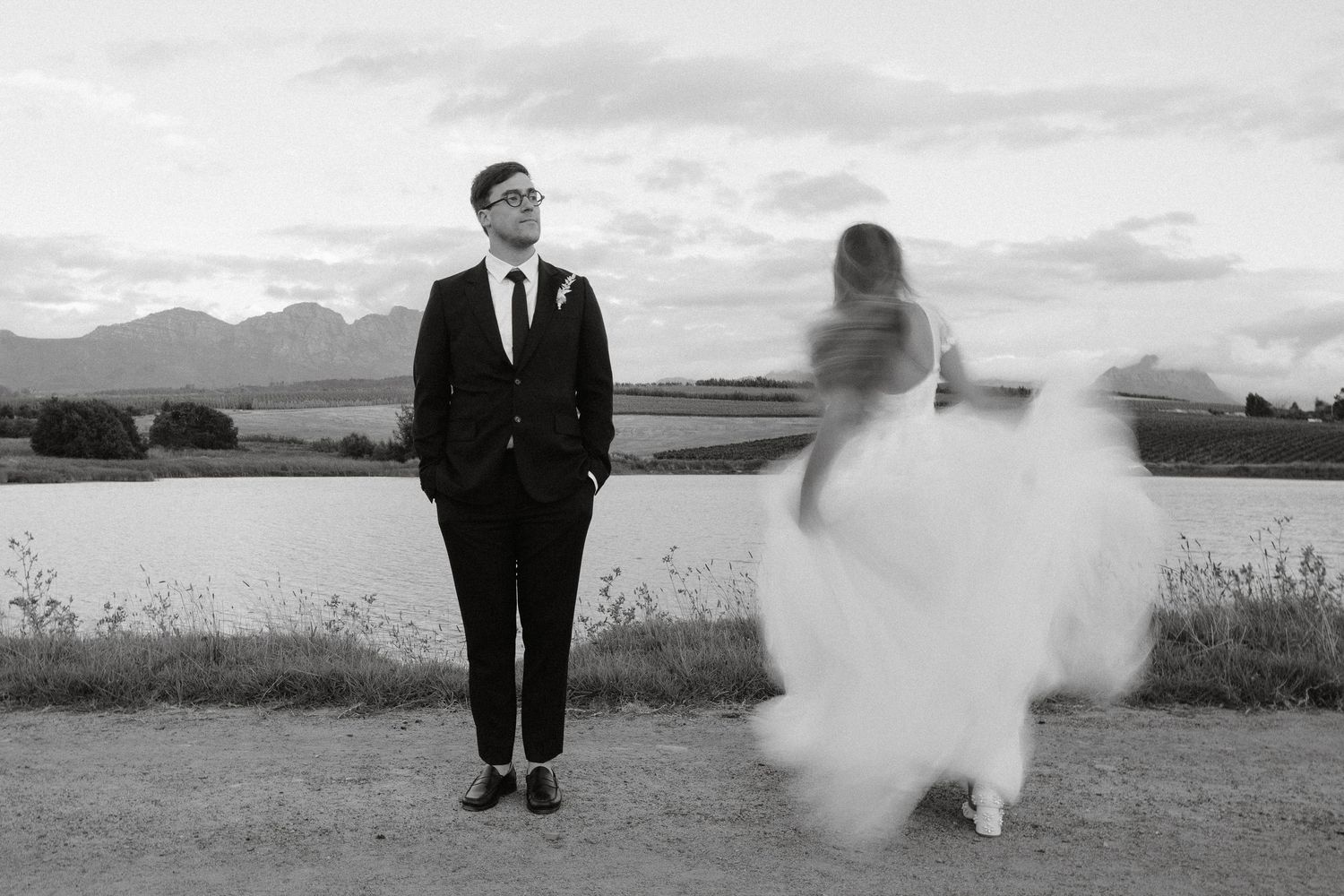 Black and white artistic wedding photography composition featuring a dramatic cloudy sky and panoramic landscape view.